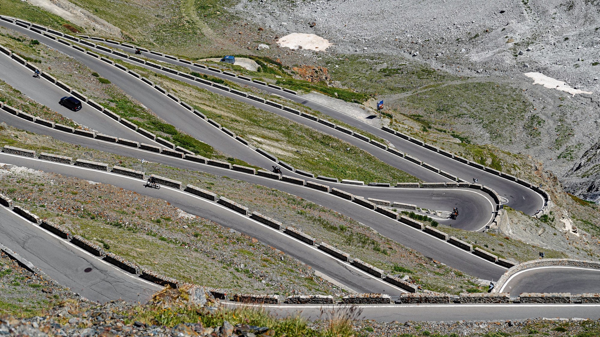 Aerial view of winding mountain road cutting sharp hairpin switchbacks through green peaks