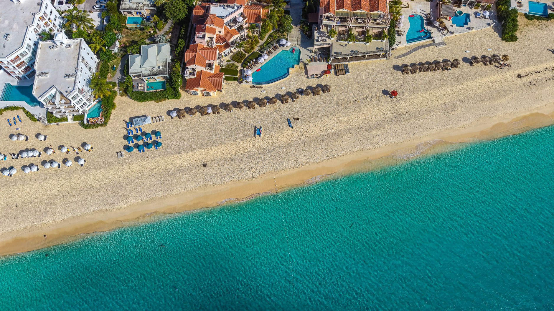 Overhead view of shallow turquoise reef waters meeting white coral sand along Anguilla's coastline