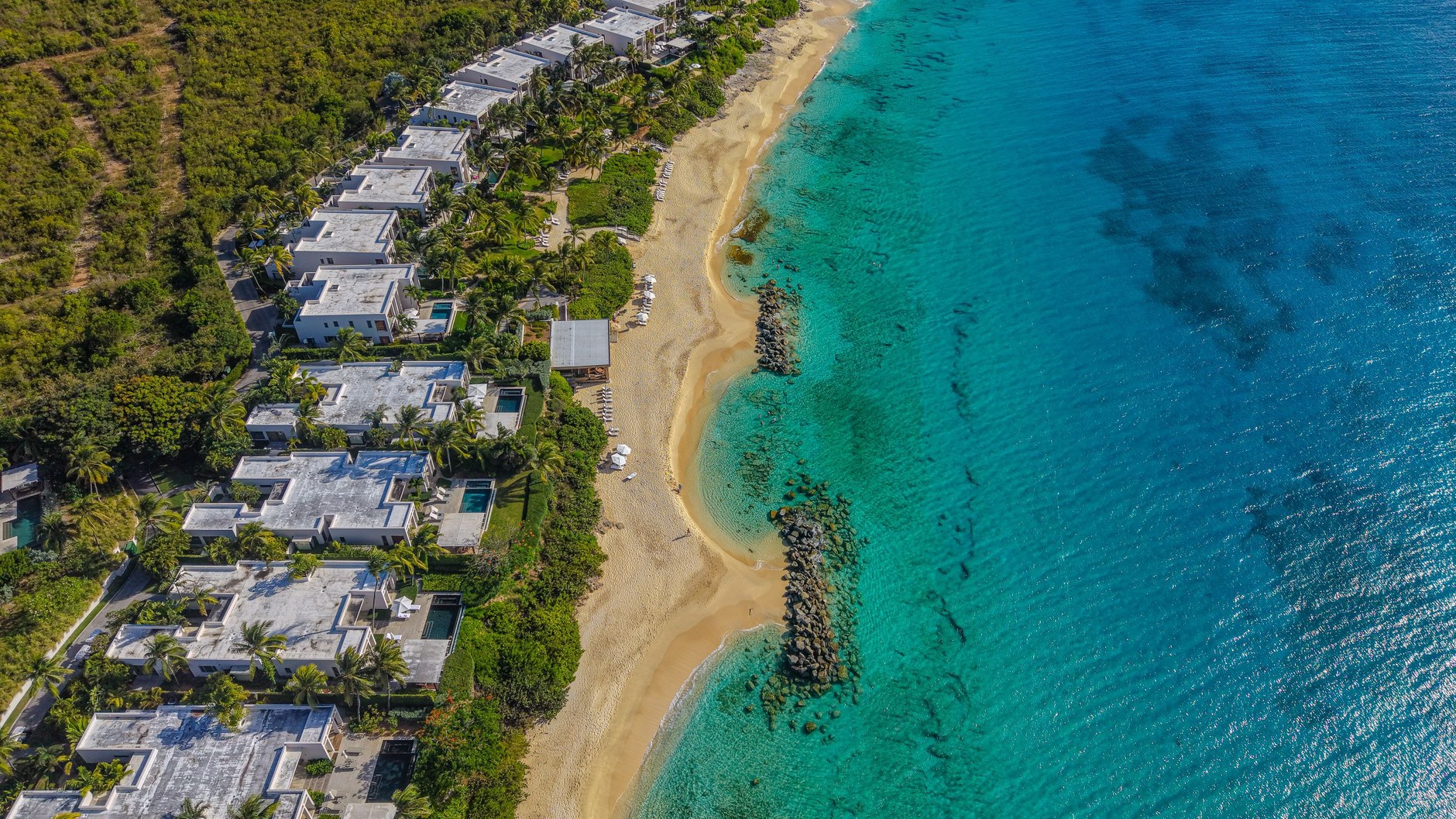 Low-rise white architectural villas situated along the turquoise coastal waters of Anguilla