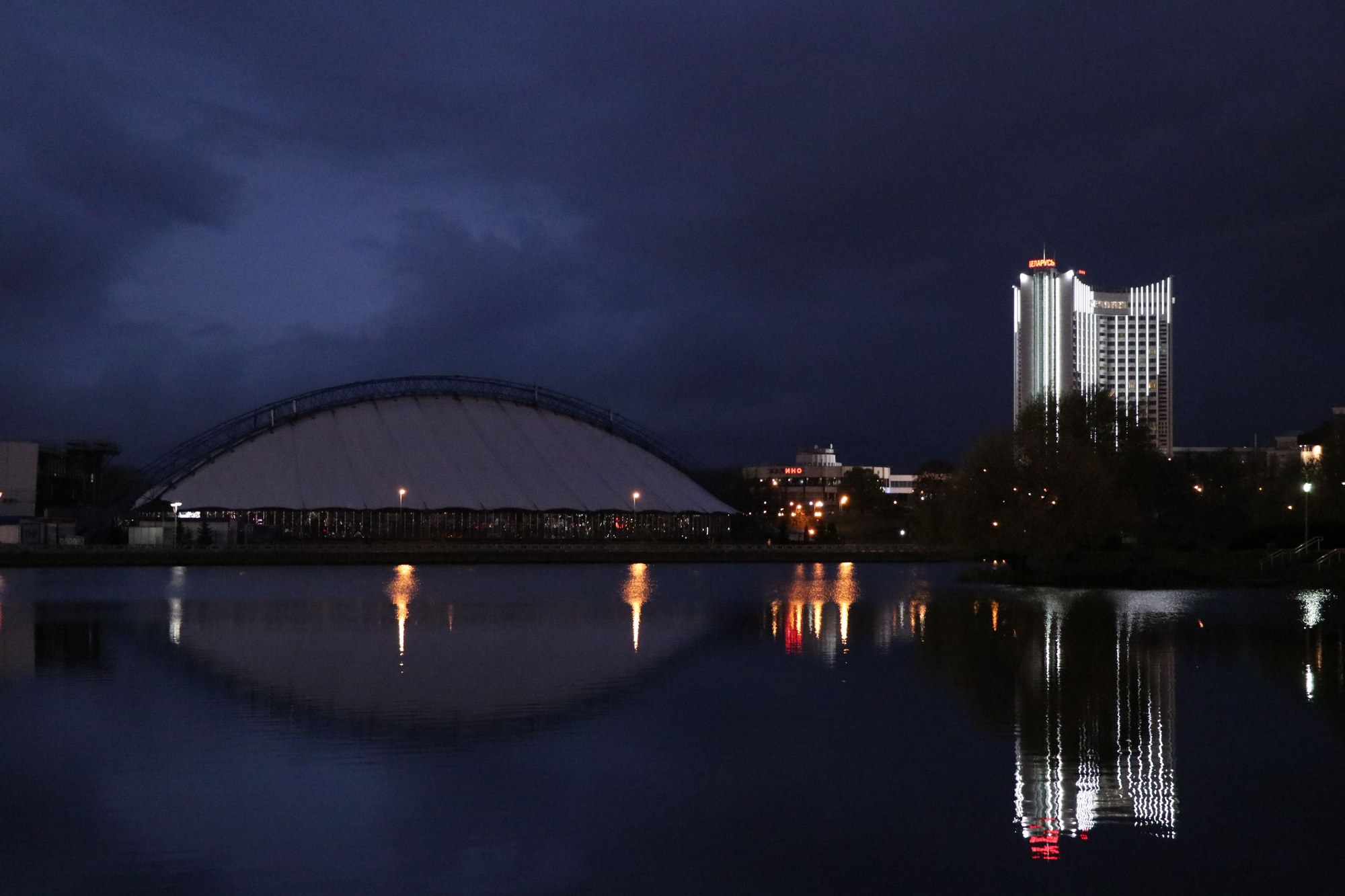 Illuminated waterfront buildings reflecting across the calm waters of the Svislach River at twilight in Minsk