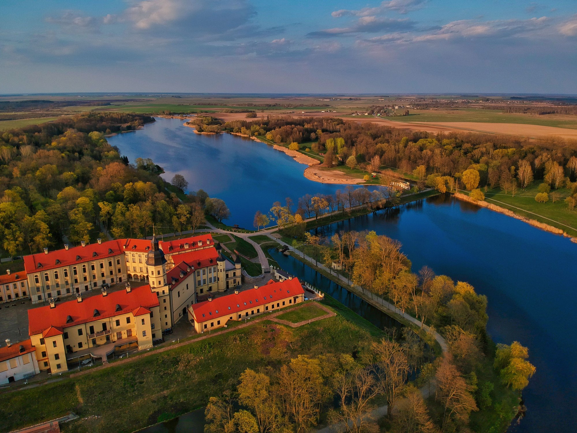 Aerial view of the red-roofed Nesvizh Castle estate surrounded by calm river waters and parklands in Belarus