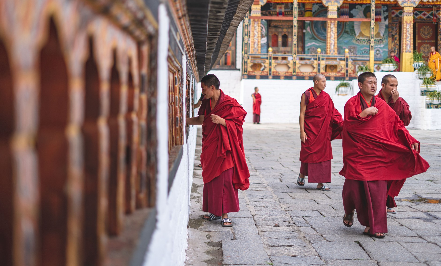 Buddhist monks draped in traditional maroon robes conversing inside an ornate Bhutanese monastery courtyard