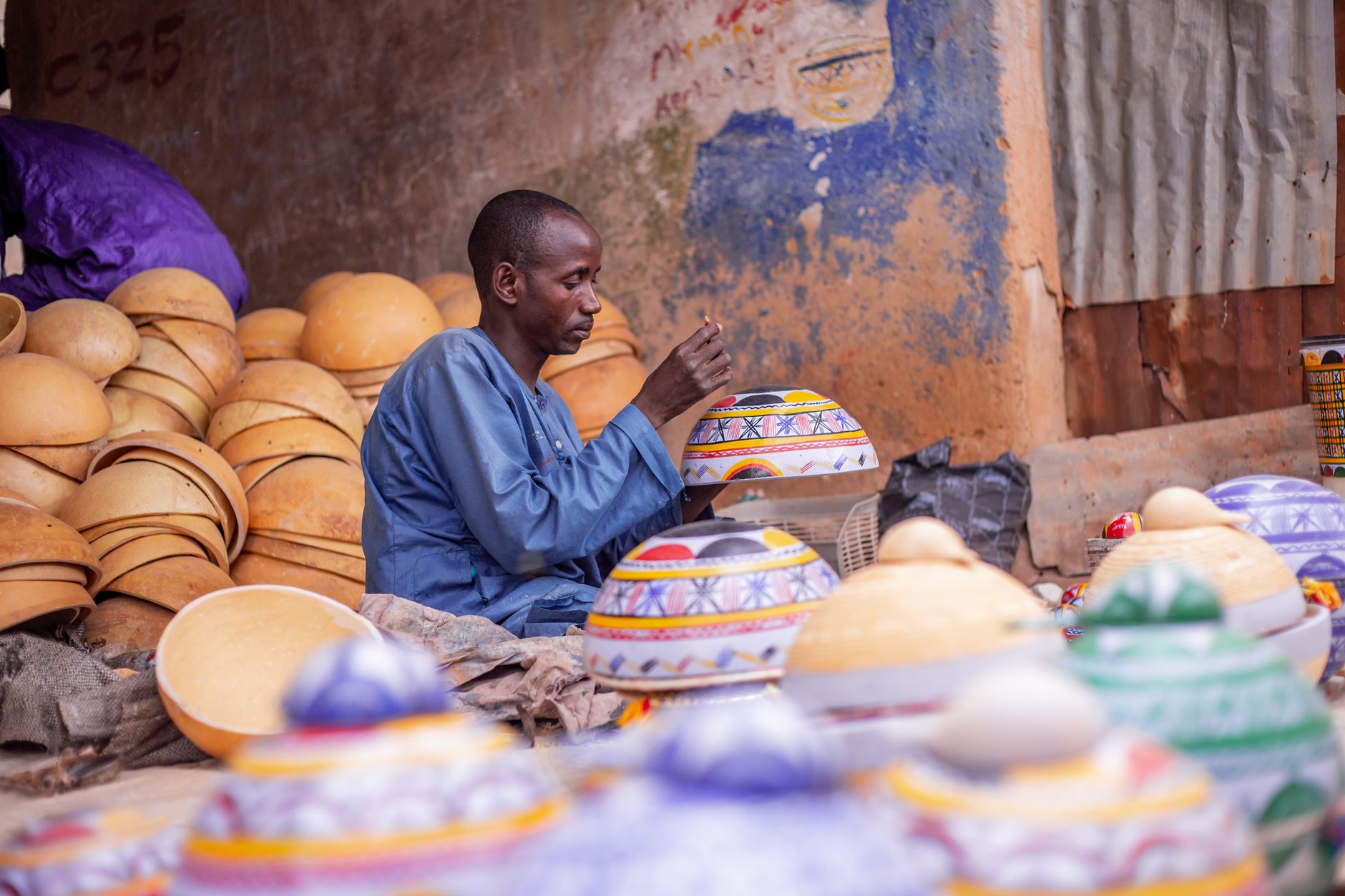 Artisan hand-painting intricate patterns on traditional terracotta pottery in an open-air workshop