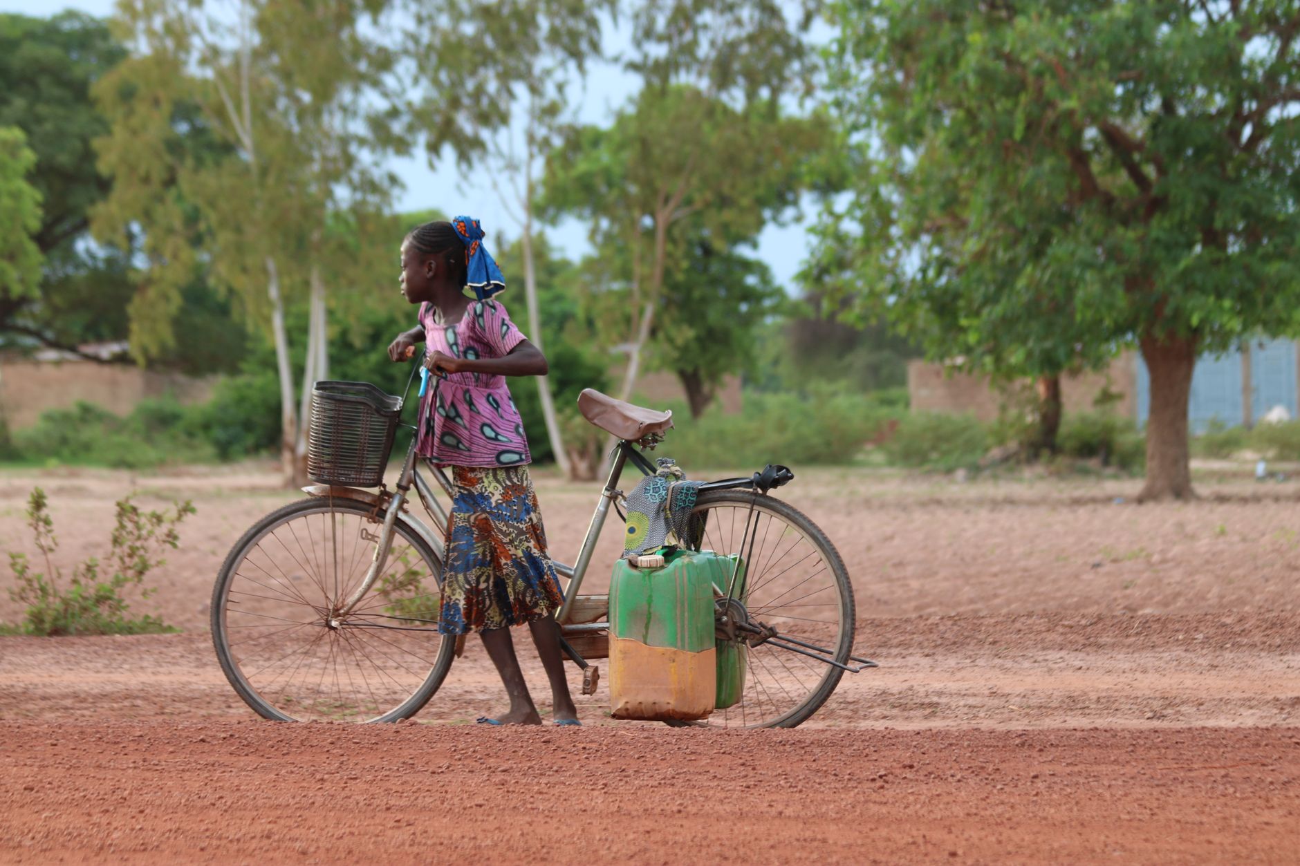 Young local girl pushing a loaded bicycle along a rural dirt road through the Burkinabé countryside