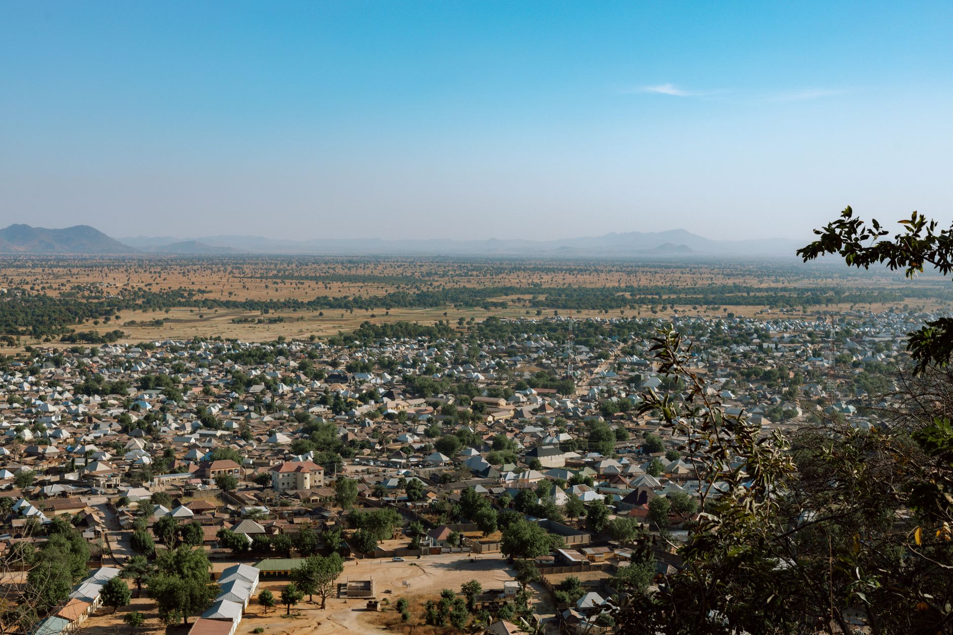 Aerial perspective of a sprawling Sahelian town with low-rise earthen structures under an expansive pale sky