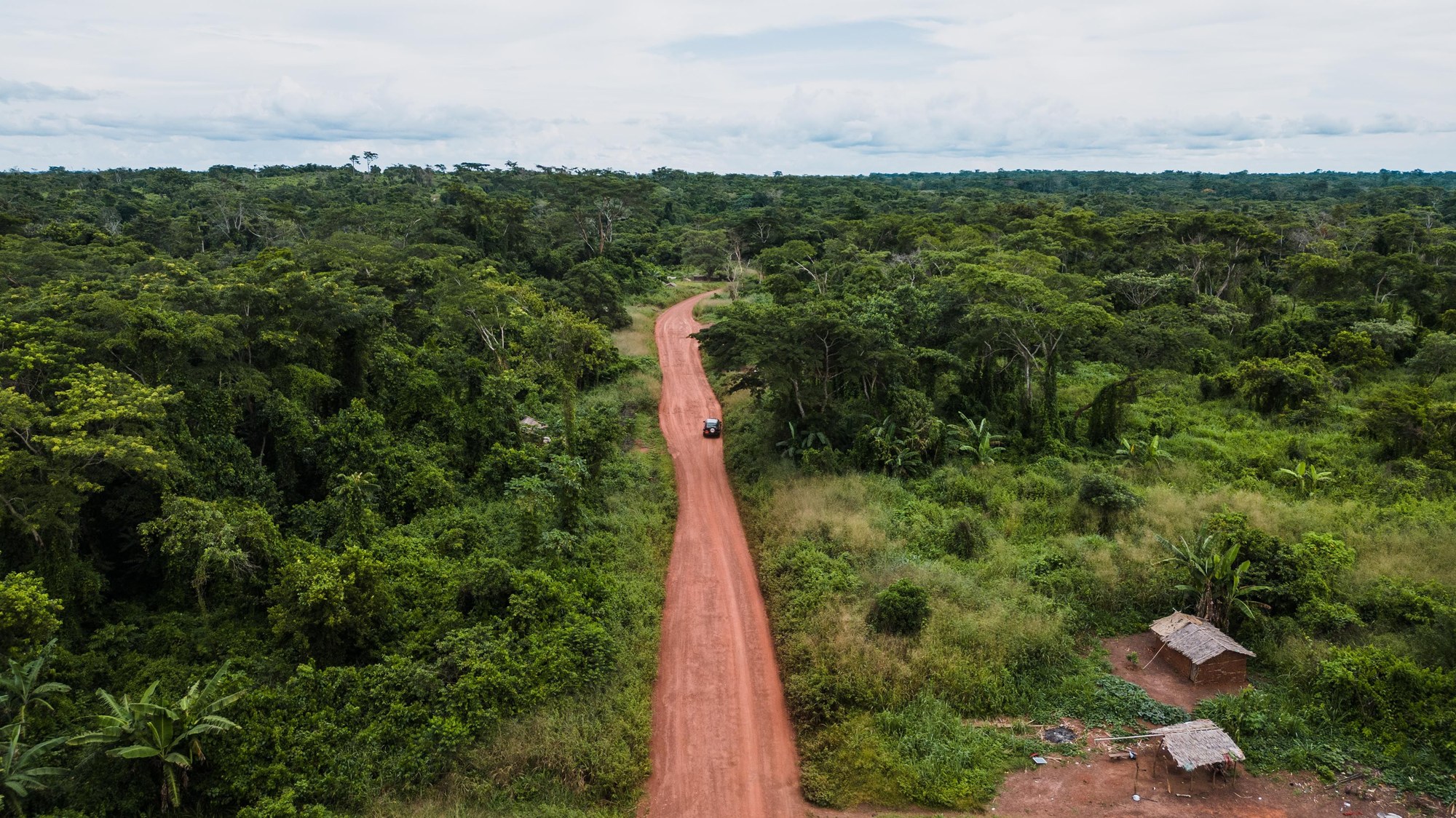 Aerial drone shot of a red dirt road cutting through deep green tropical jungle forest