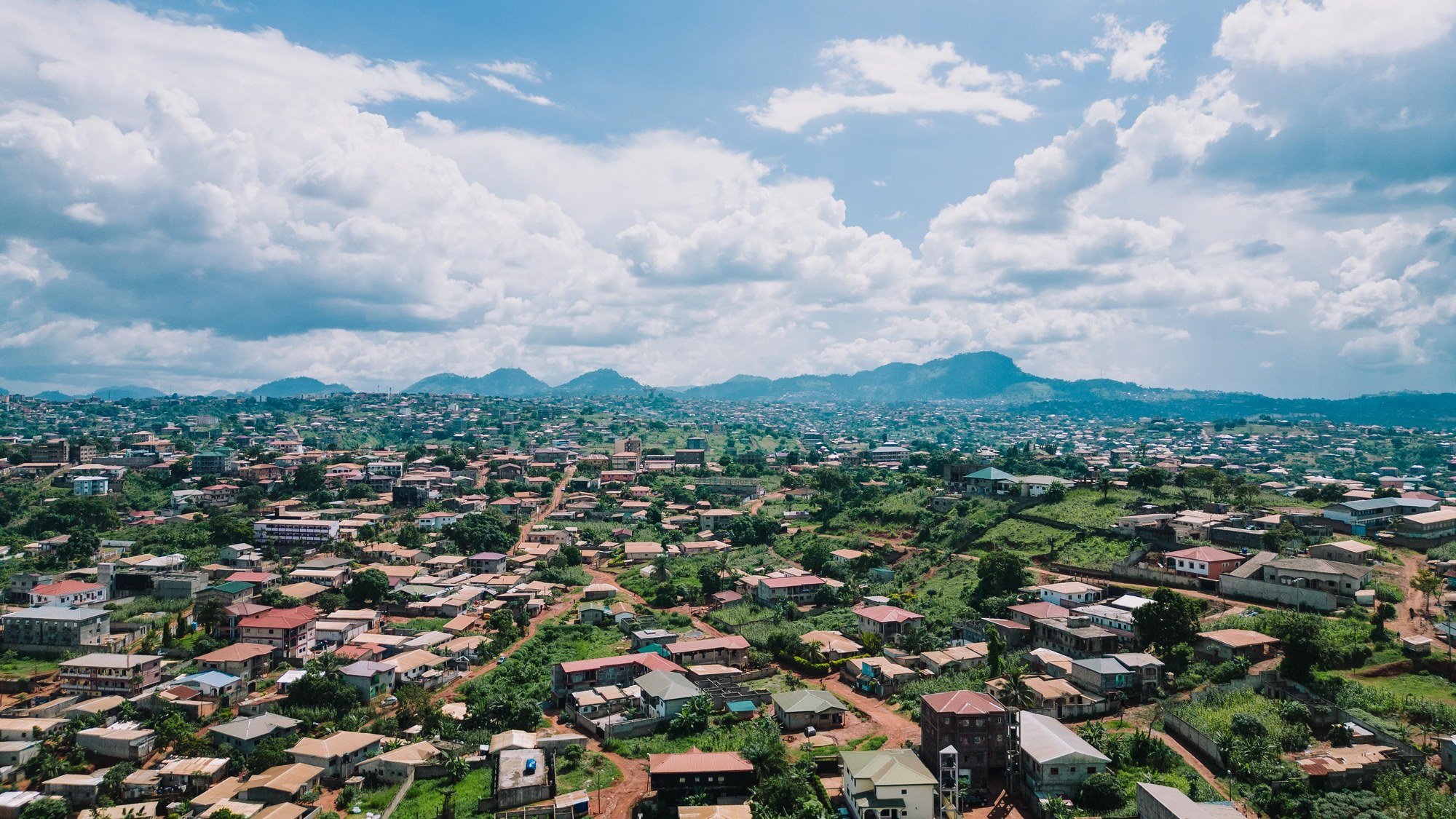 Wide drone perspective of Yaoundé buildings and green hills stretching to the horizon under daylight