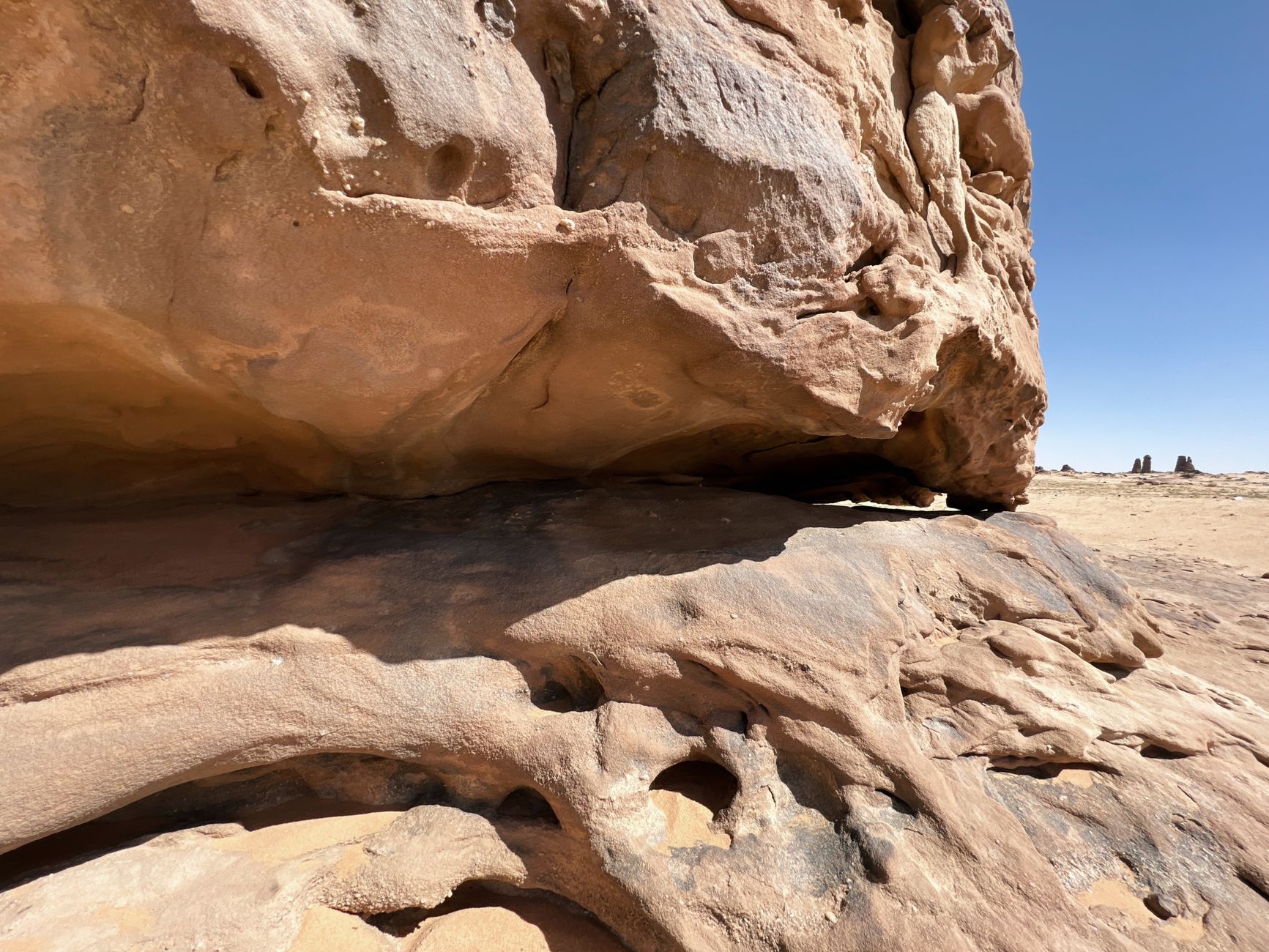 Weathered sandstone rock spires and towers rising from red desert sand under bright sunlight in Chad