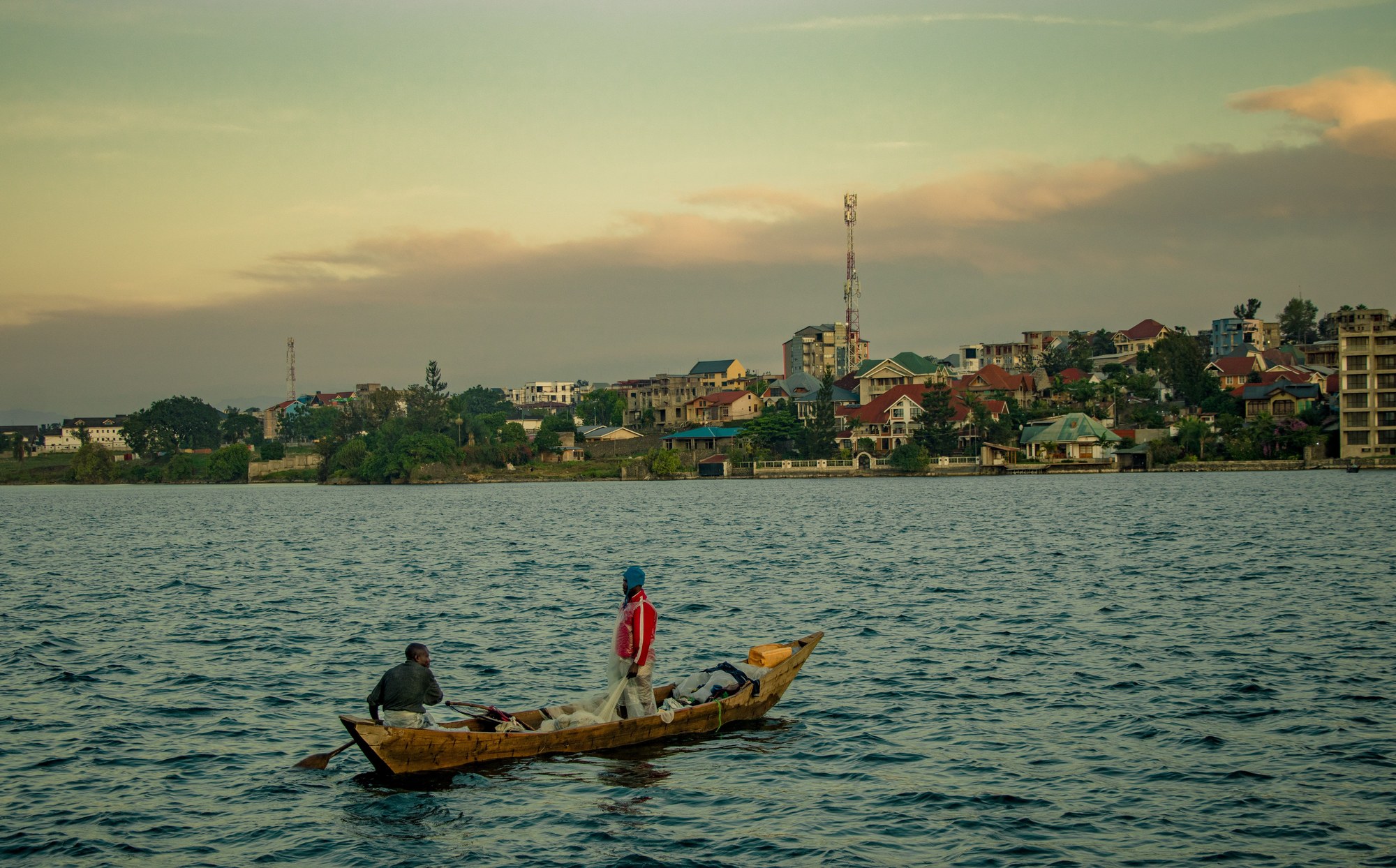 Local fishermen in traditional wooden pirogues on Lake Kivu at sunset with distant green hills