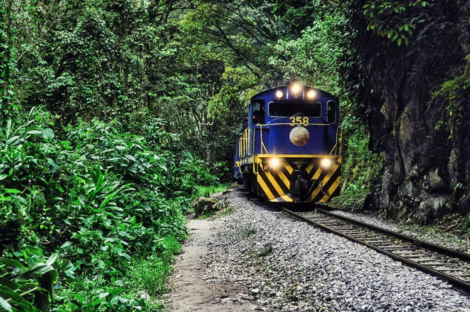Railway tracks cutting through dense equatorial rainforest toward interior plateau ridges