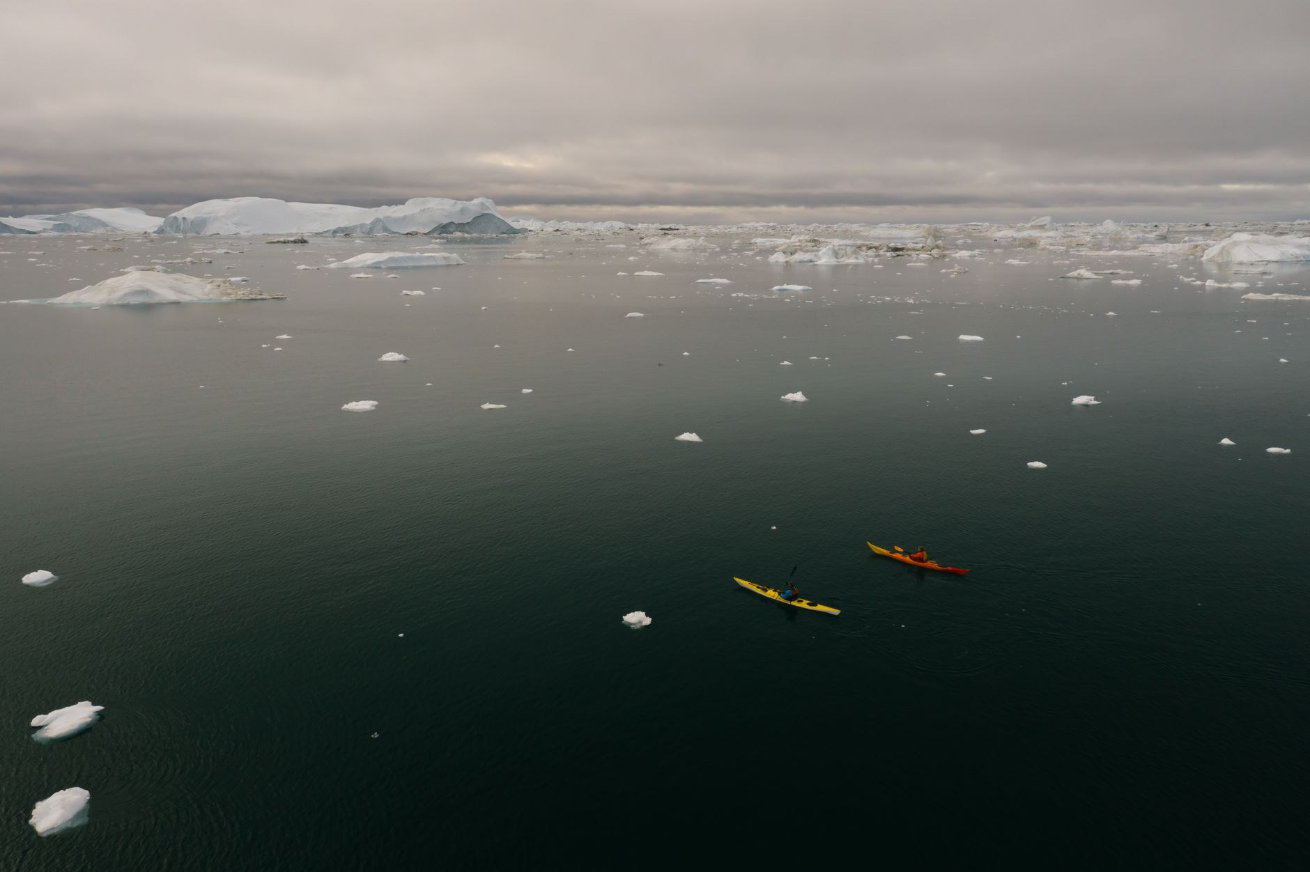 Sea kayaker navigating calm waters near icebergs in Disko Bay