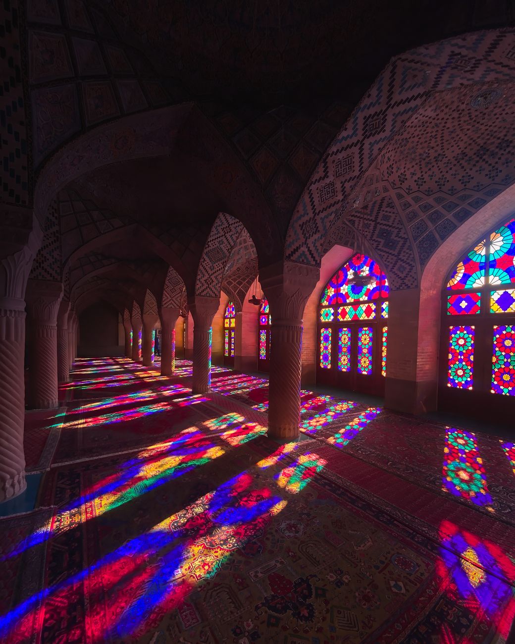 Morning sunlight streaming through polychromatic stained glass windows onto ornate Persian carpets inside Nasir al-Mulk Mosque in Shiraz
