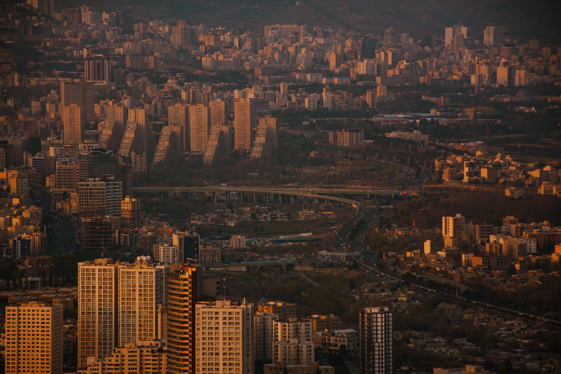 Modern urban cityscape of Tehran with high-rise buildings set against the dramatic snow-capped Alborz mountain range at dusk