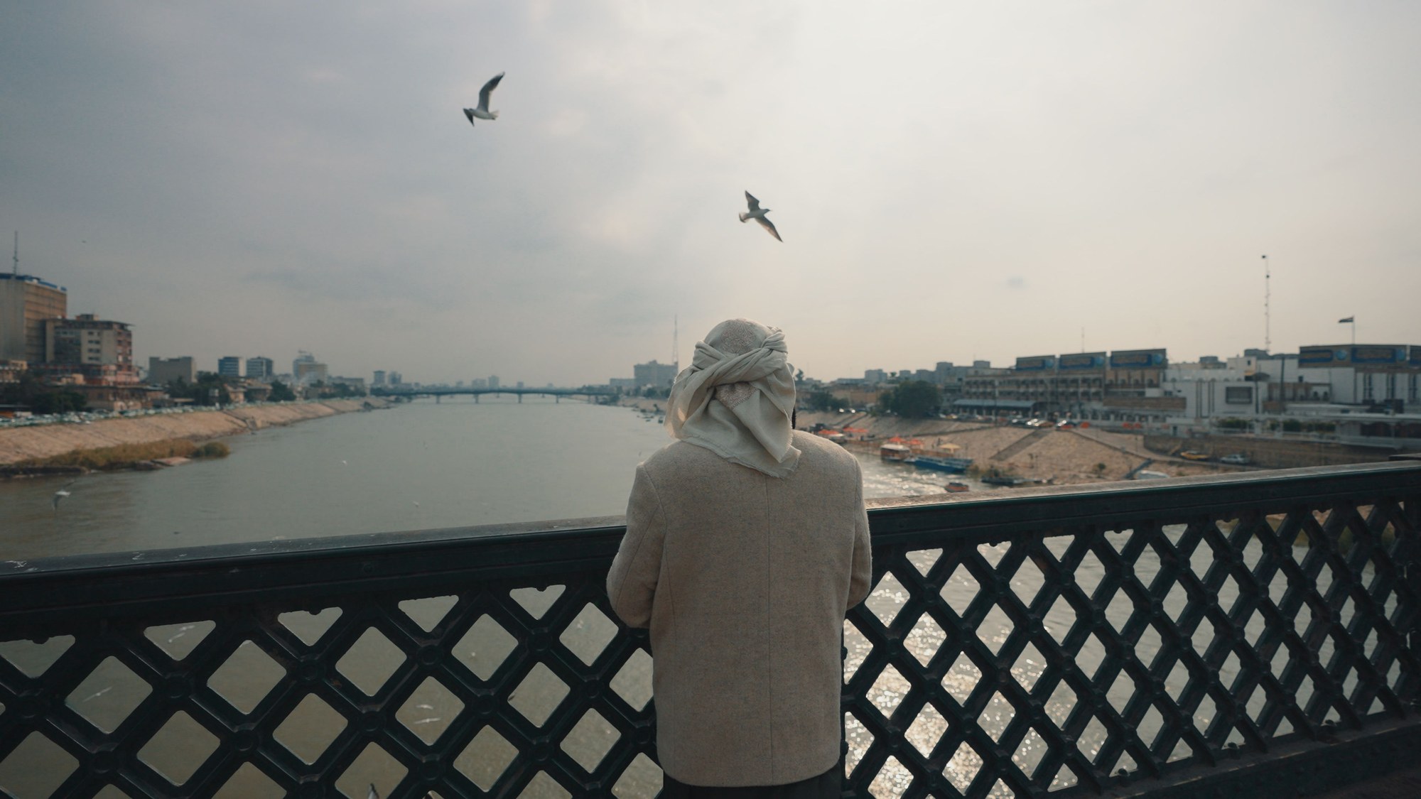 Pedestrian looking out across the broad waters of the Tigris River from an urban bridge in central Baghdad