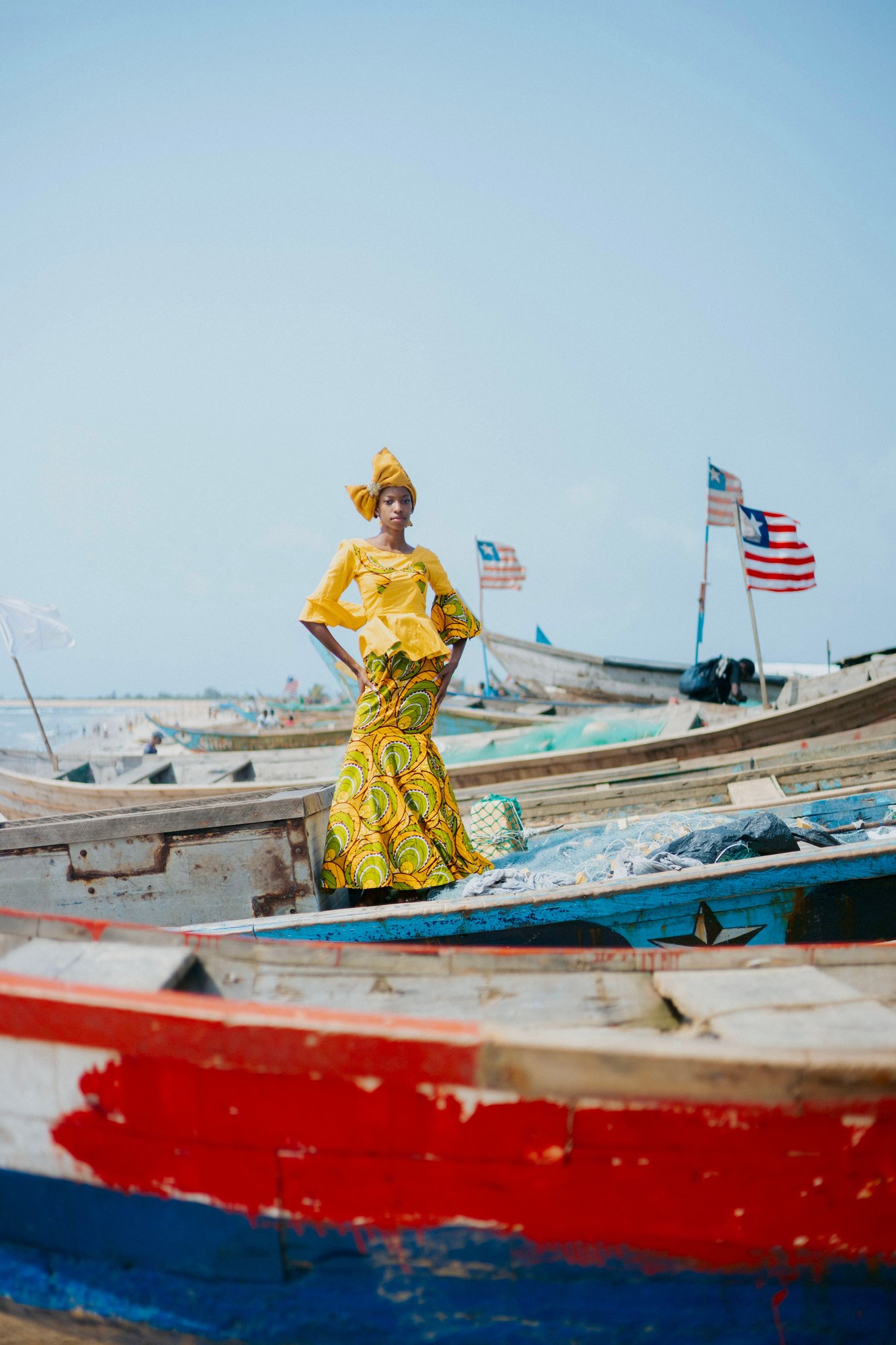 Woman in colorful traditional West African fabric standing by wooden fishing canoes in Monrovia