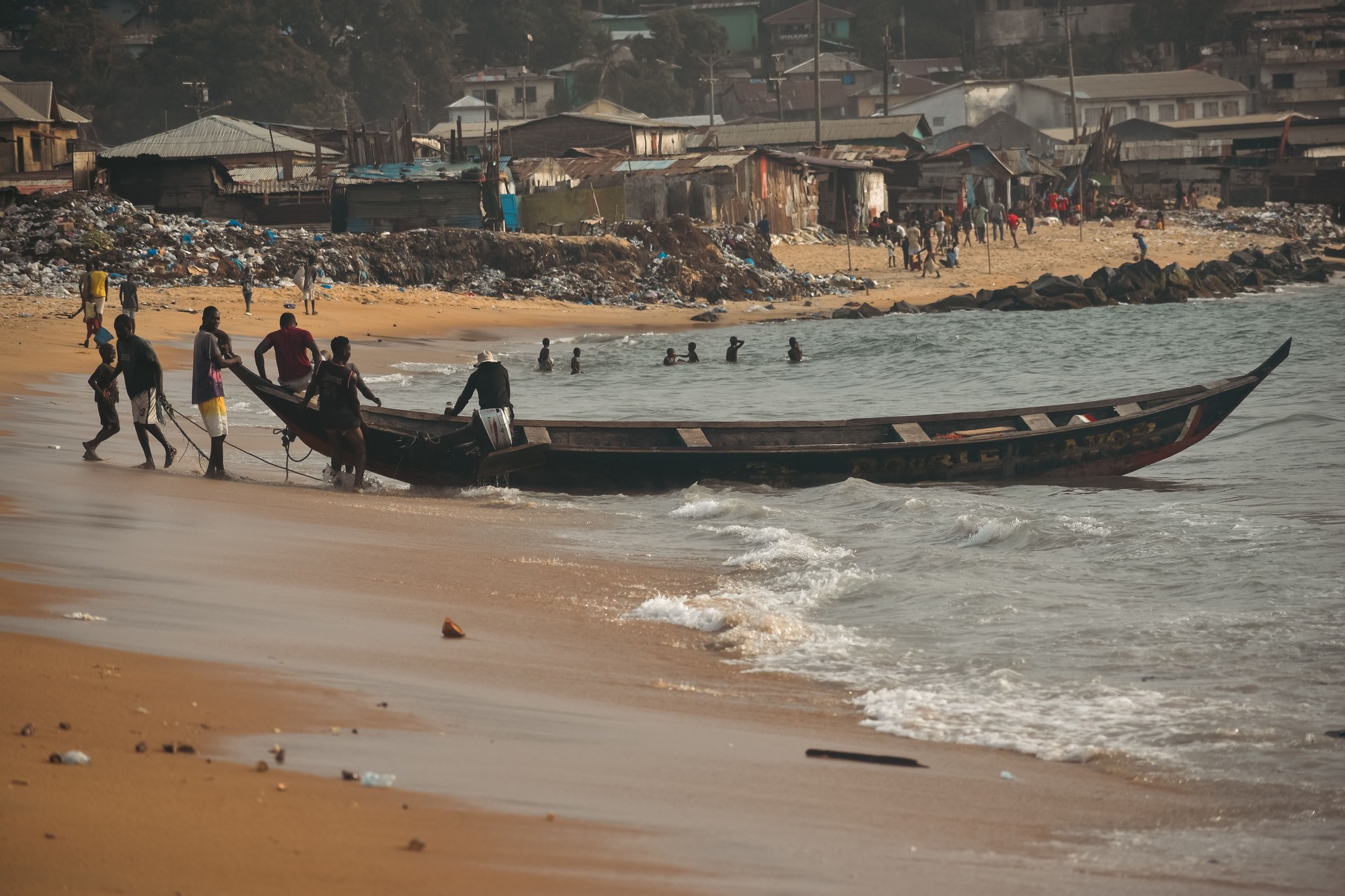 Artisanal fishermen pulling their wooden dugout canoe ashore through Atlantic surf in Monrovia