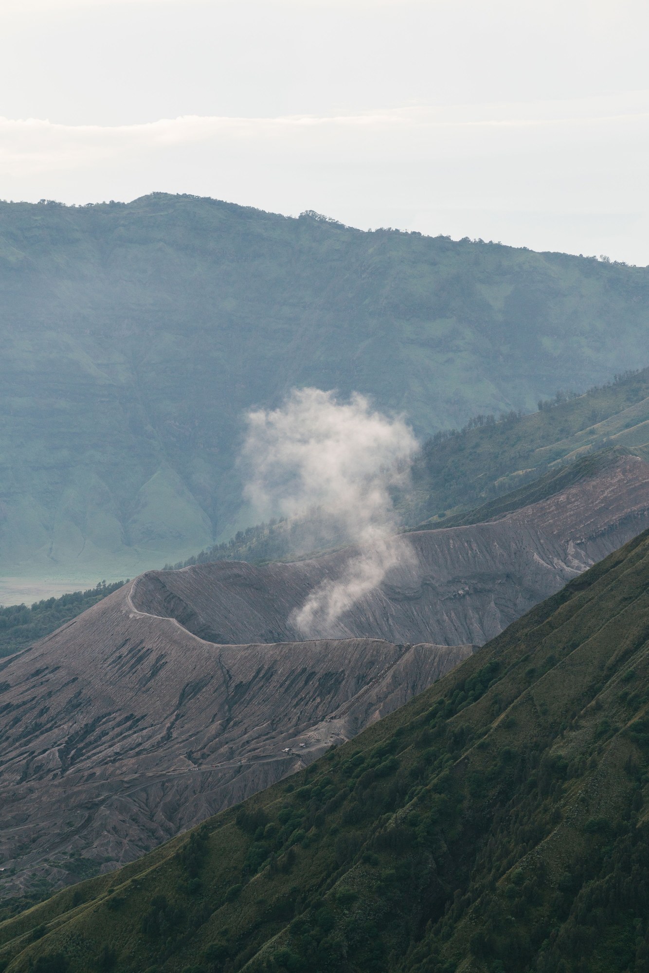 Steaming volcanic crater and rocky mineral deposits among mountain slopes