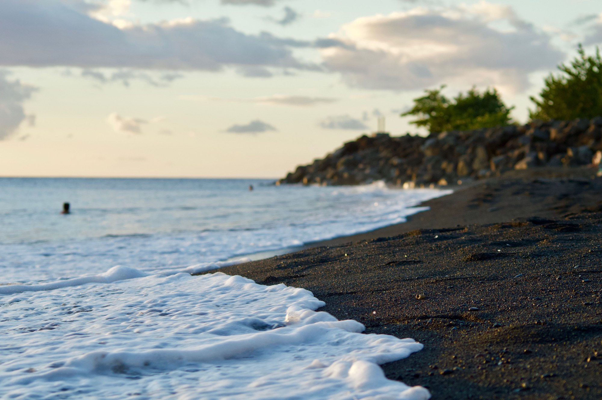 Gentle ocean waves washing over dark black volcanic sand beach