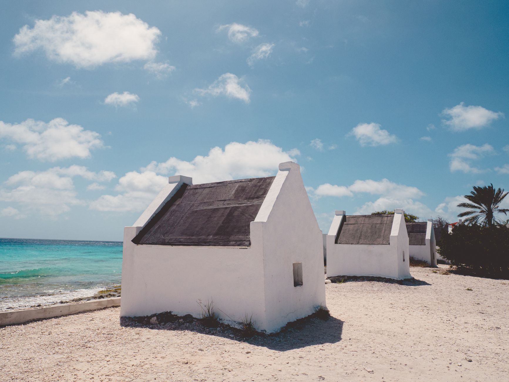 Row of historic stone slave quarters and huts built in 1850 along the turquoise ocean shoreline of southern Bonaire