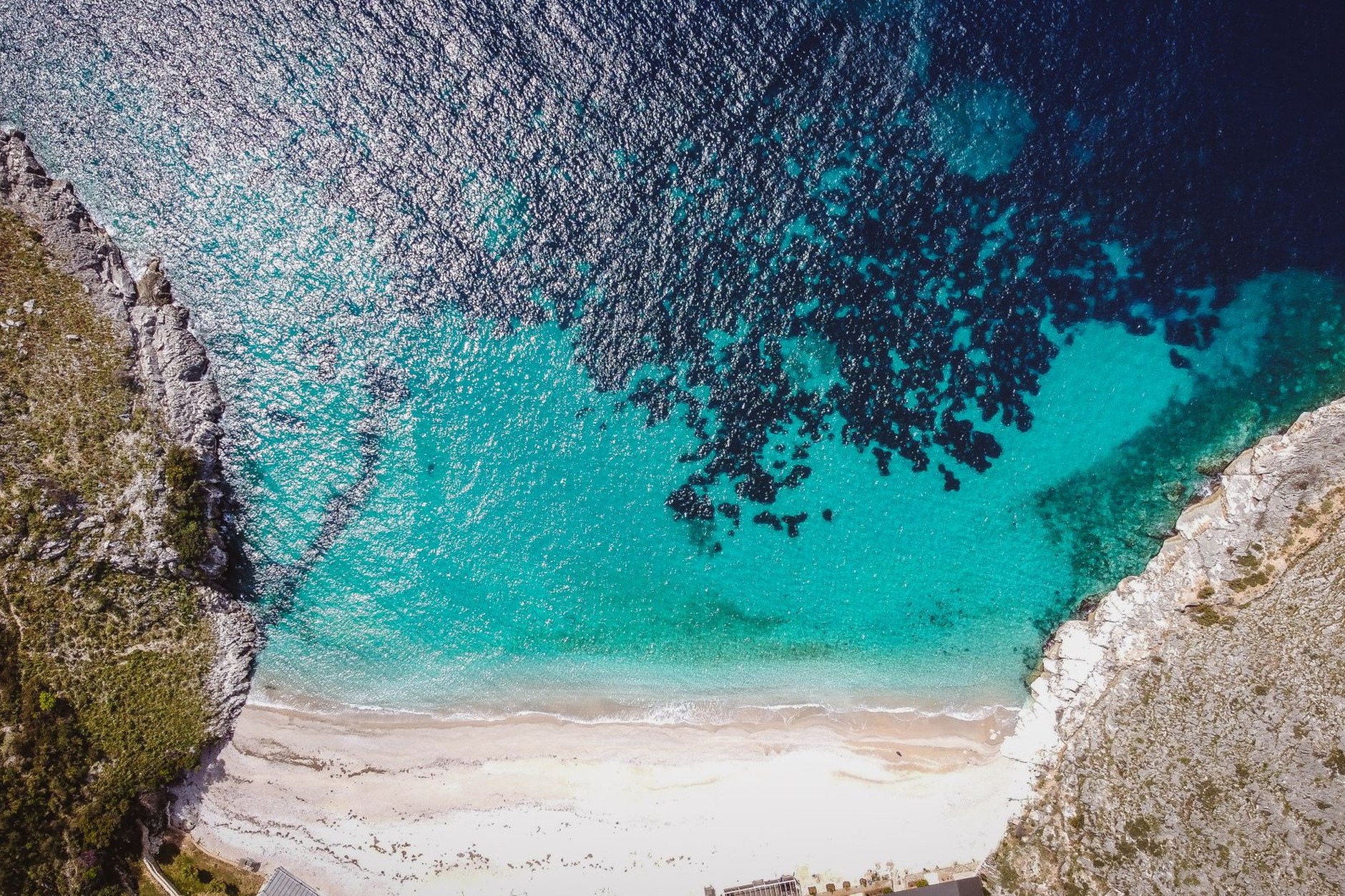 Secluded white pebble cove and turquoise sea framed by the towering vertical red cliffs of Gjipe Canyon in Albania