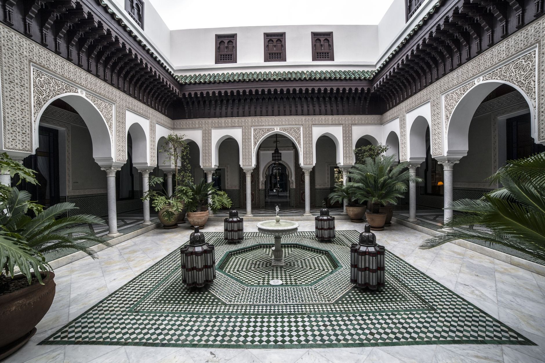 An ornate palace courtyard with painted arches, intricate ceramic tiles, and fragrant orange trees in Constantine