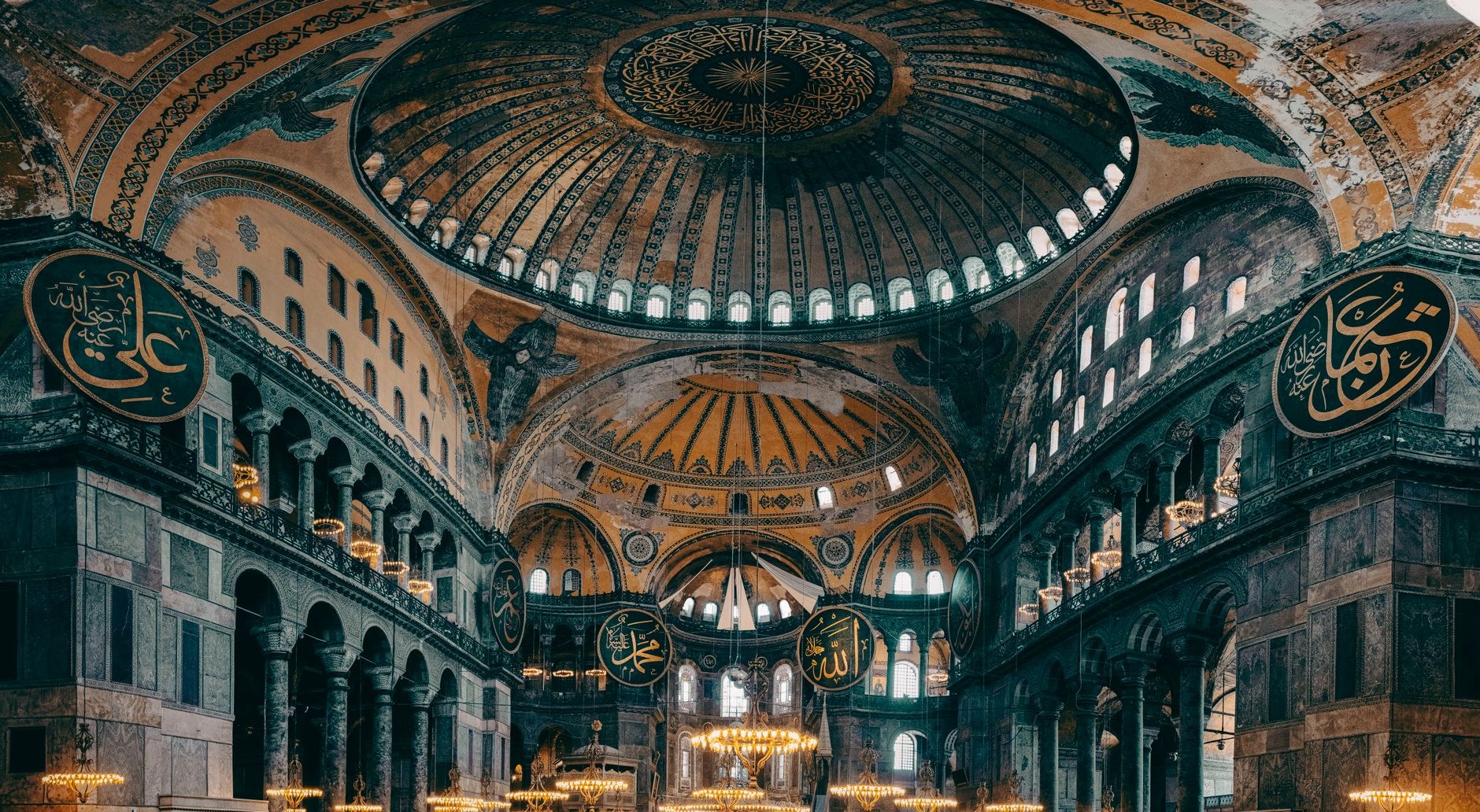 A neo-Byzantine stone basilica with decorative blue domes perched on a high cliff overlooking the Mediterranean