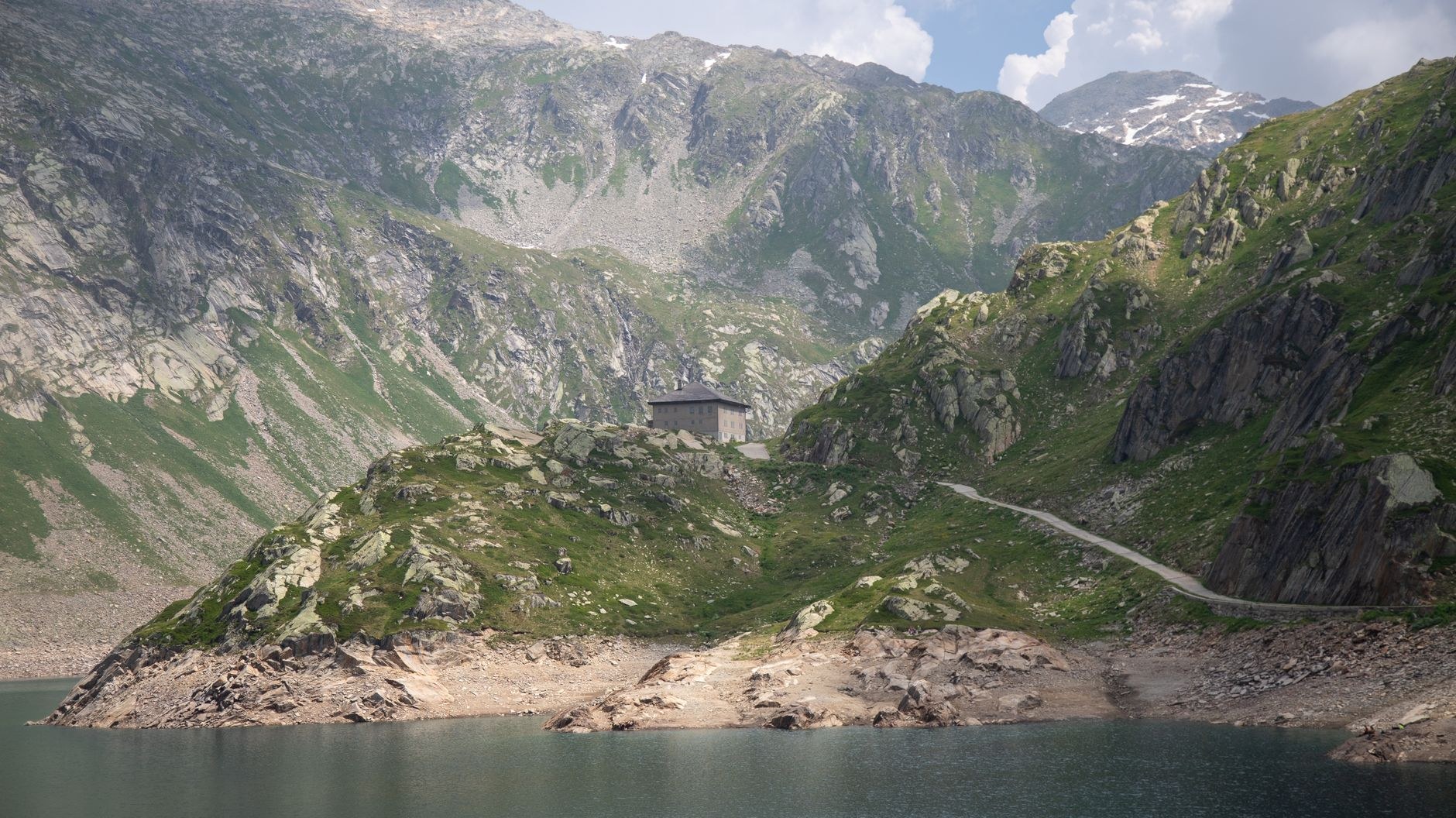 A rocky hiking path following a mountain stream through an expansive glacial valley dotted with stone huts