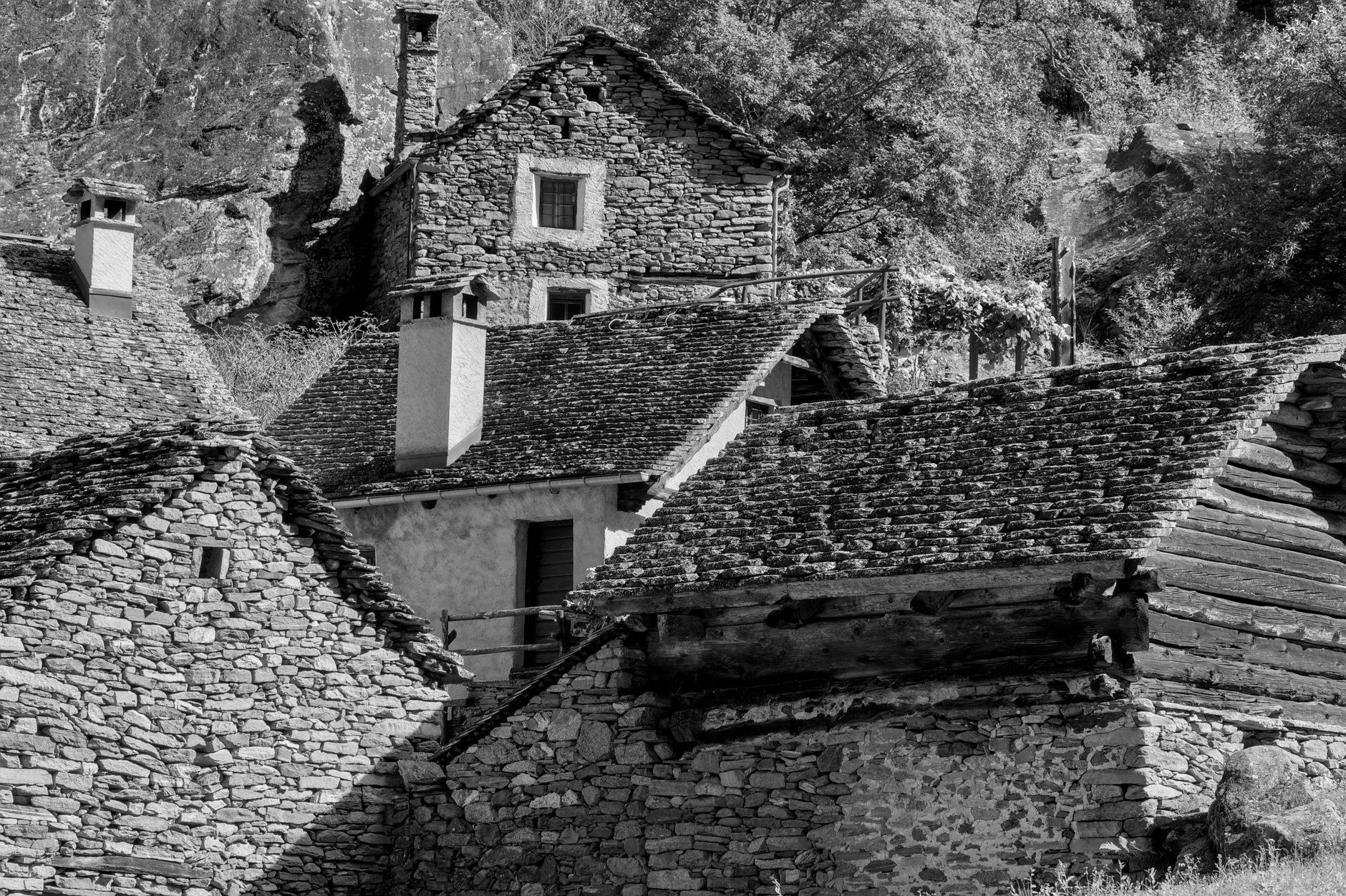 Charming rustic stone houses with dark slate roofs and wooden balconies along a steep mountain lane
