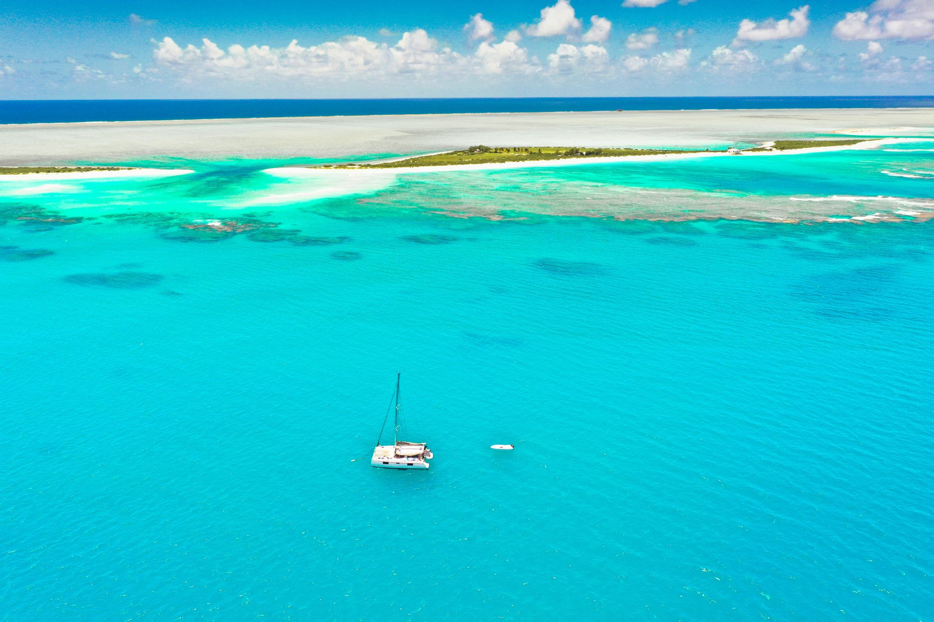 Aerial view of an untouched long sandy barrier spit bordered by shallow turquoise ocean waters