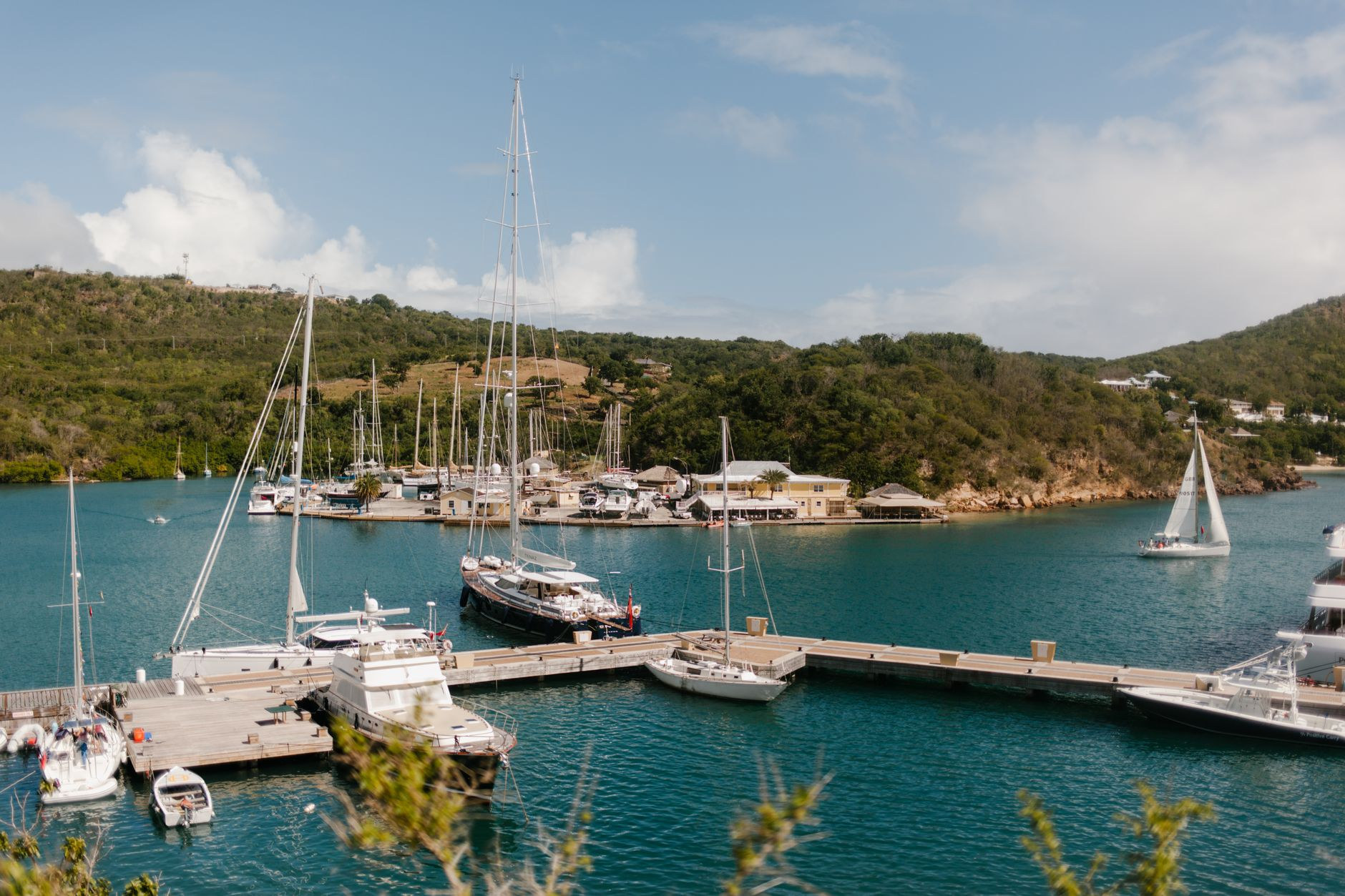 Sailing yachts and catamarans moored along stone quays beneath forested coastal headlands at a Caribbean colonial marina