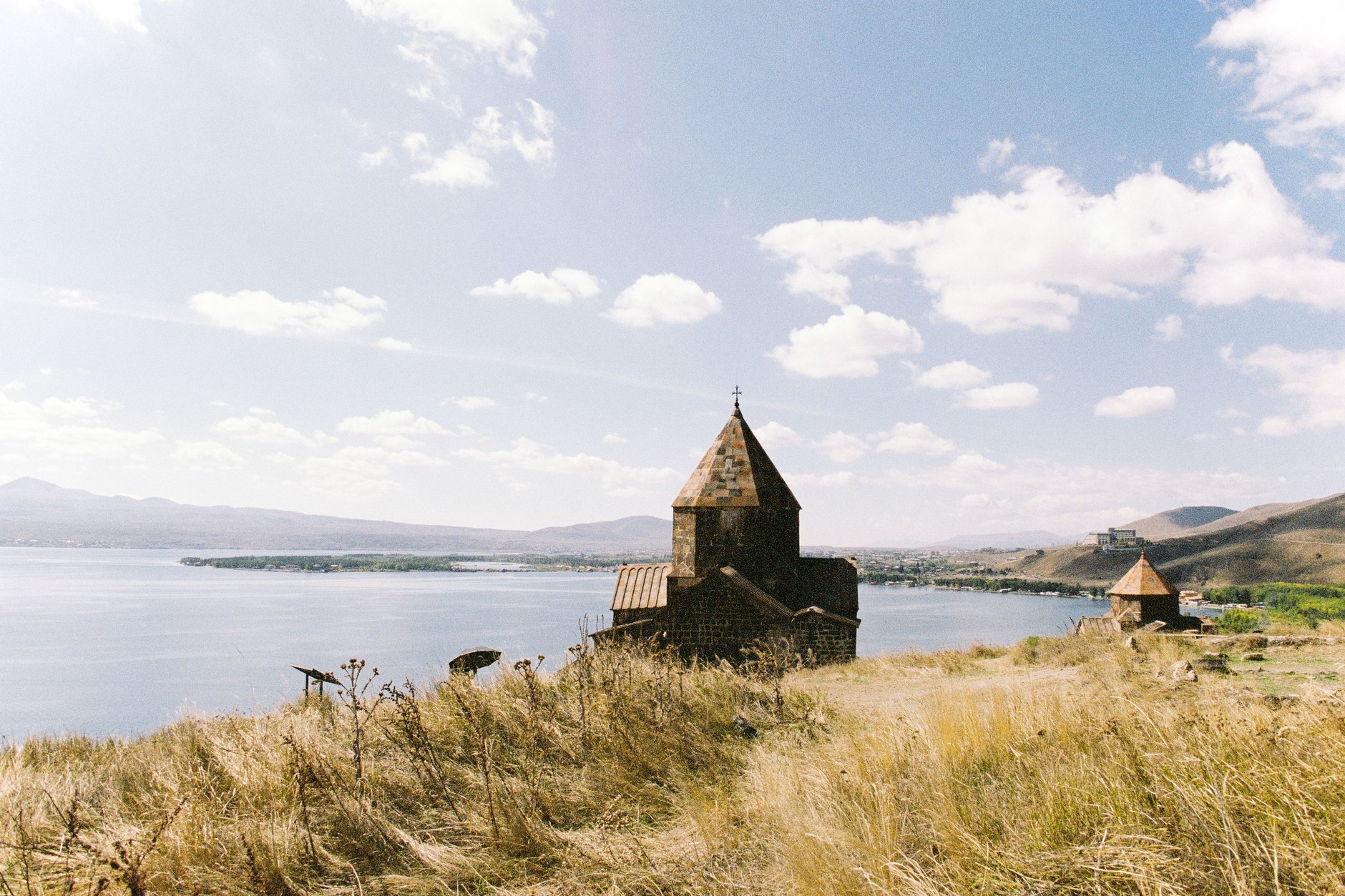 Twin black tuff stone churches of Sevanavank monastery perched on a hill above the turquoise waters of Lake Sevan under clear skies