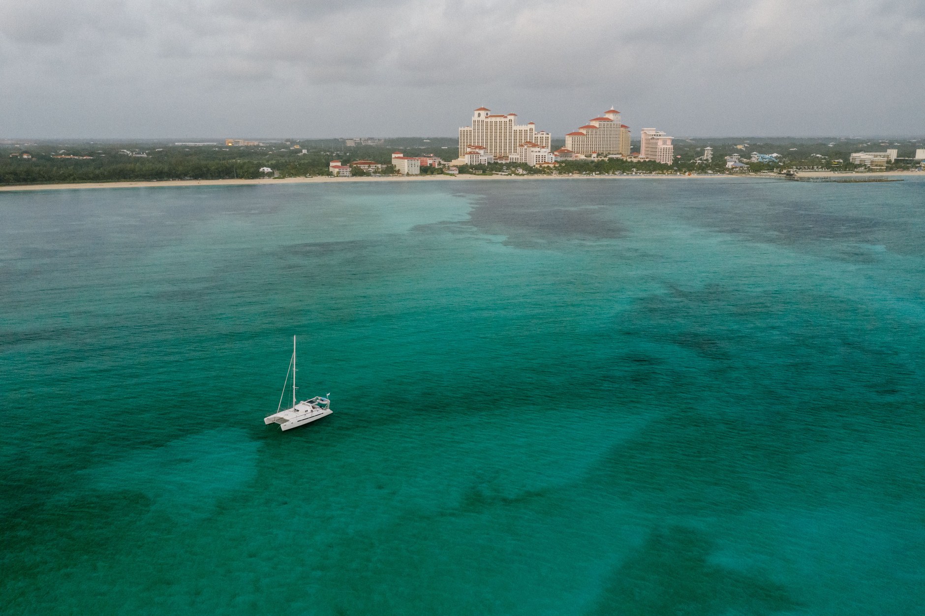 Sailboat moored in calm aquamarine waters off a natural barrier island shoreline in the Bahamas