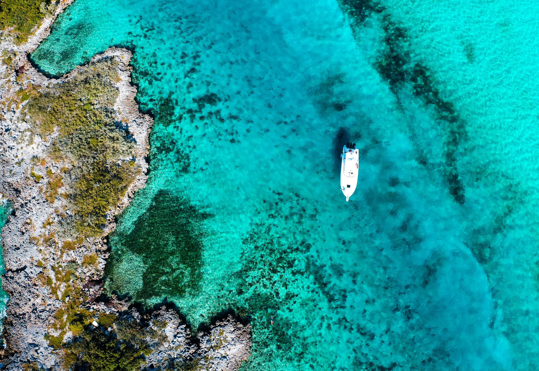 Aerial view of a boat cruising across translucent turquoise shallows and sand flats in the Bahamas