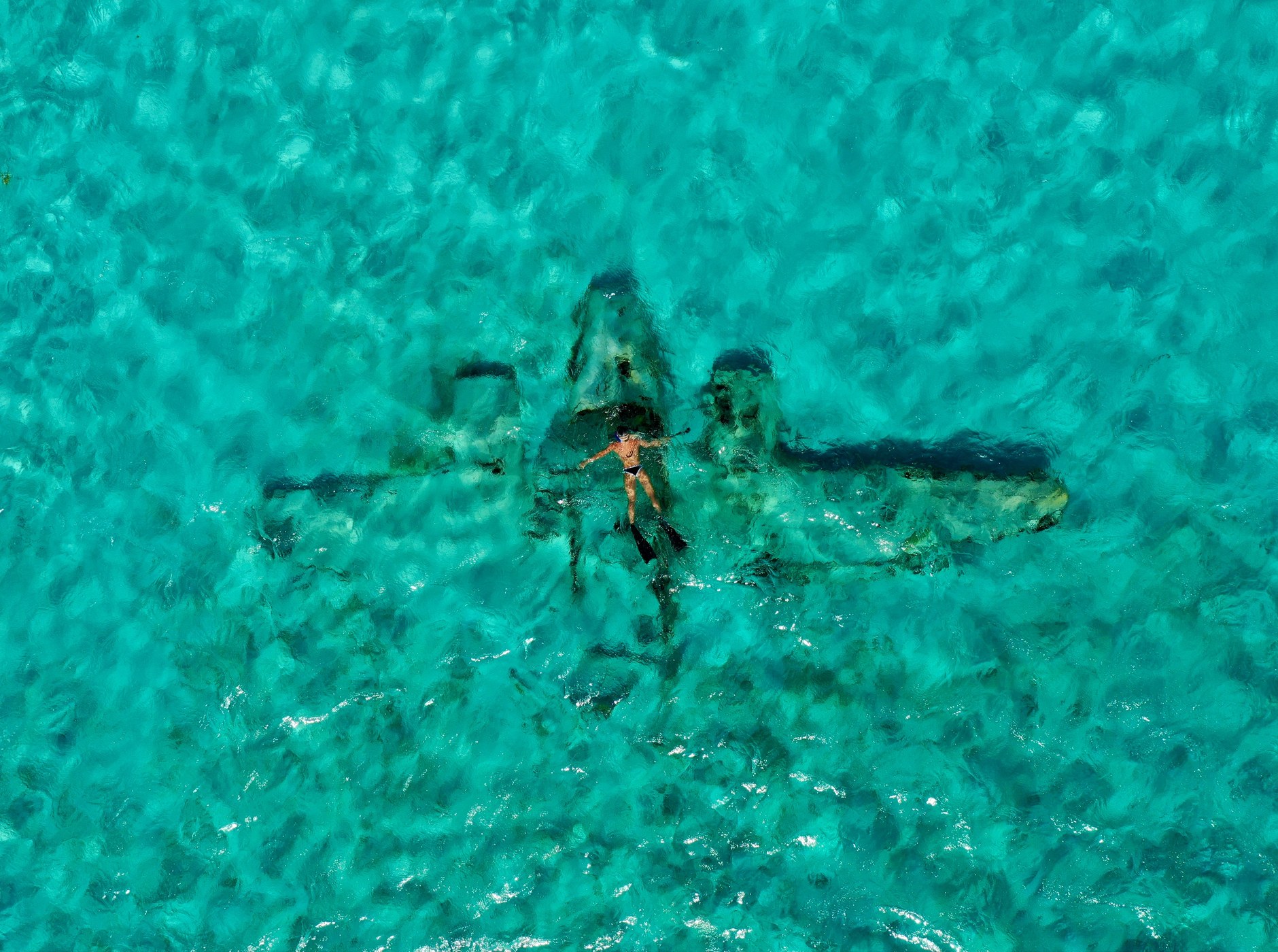 Snorkeler exploring a submerged aircraft wreck resting on shallow turquoise ocean sandbars