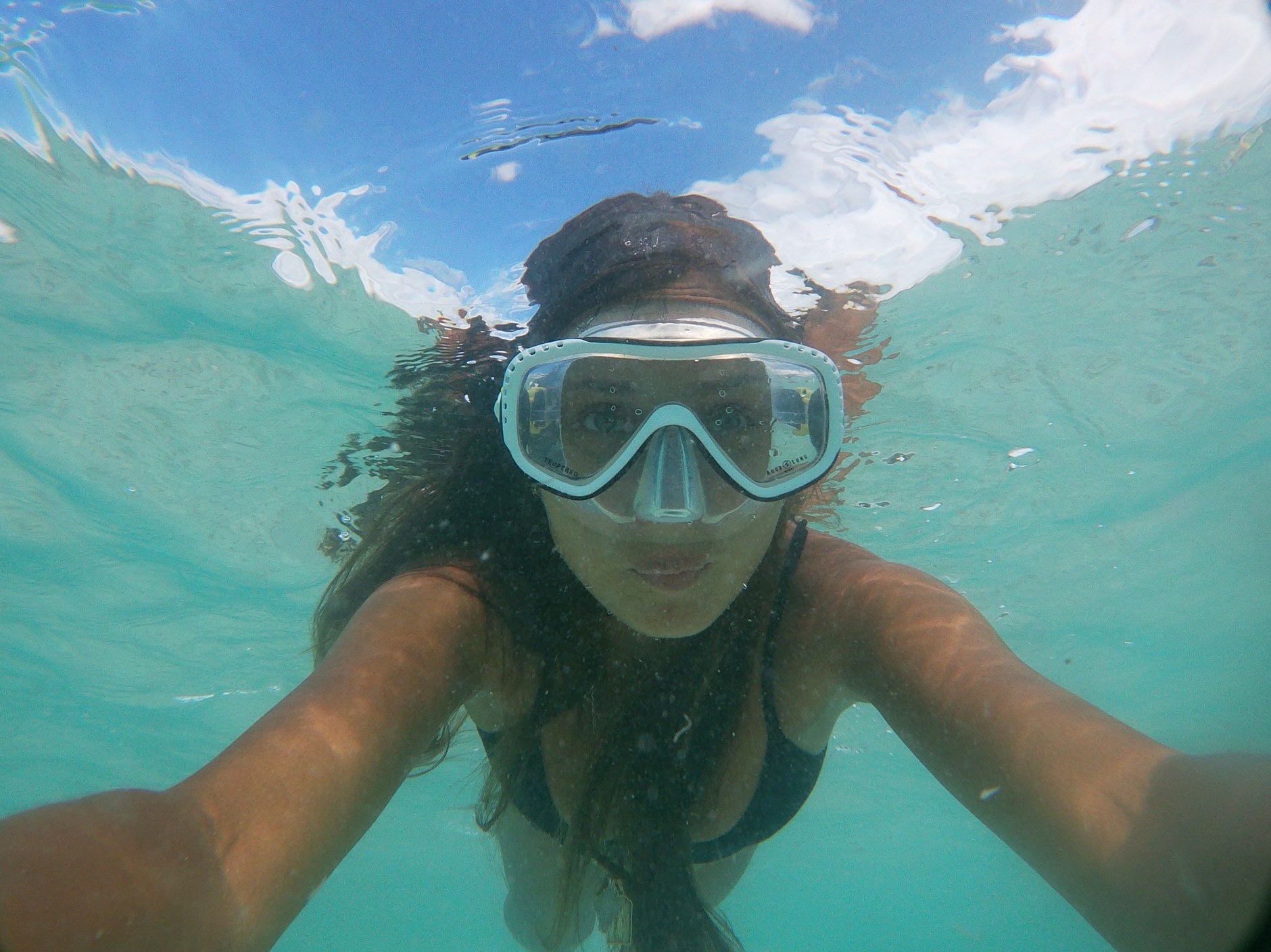 Swimmer snorkeling through clear blue ocean waters over marine life and limestone rock formations