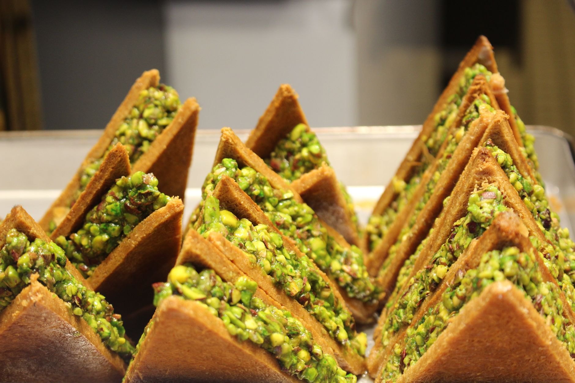 Bowl of rich glossy Bahraini halwa confectionery garnished generously with crushed green pistachios, almonds, and saffron