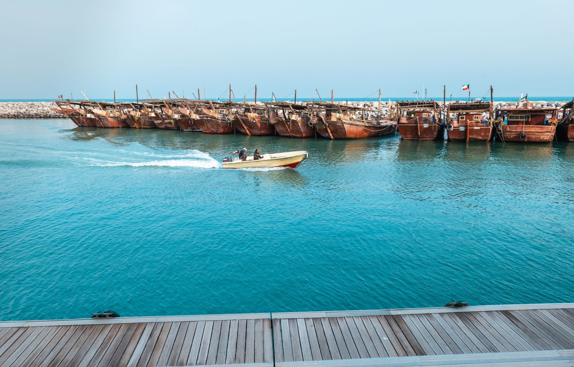 Handcrafted wooden dhow boats moored quietly along a harbor wharf with the modern city skyline across the bay