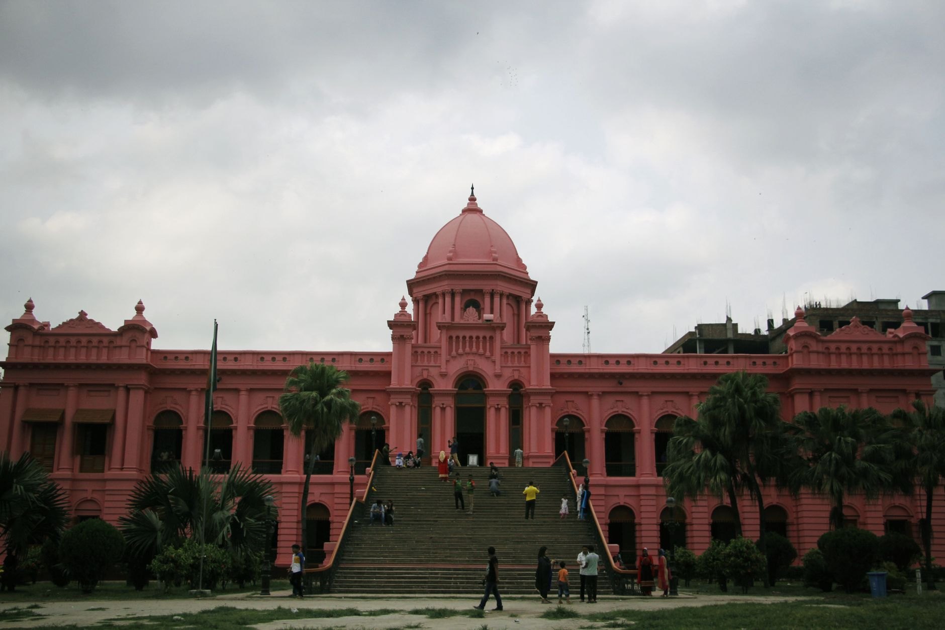 Monumental pink neo-classical facade and grand central dome of Ahsan Manzil facing palm gardens on the Buriganga riverbank
