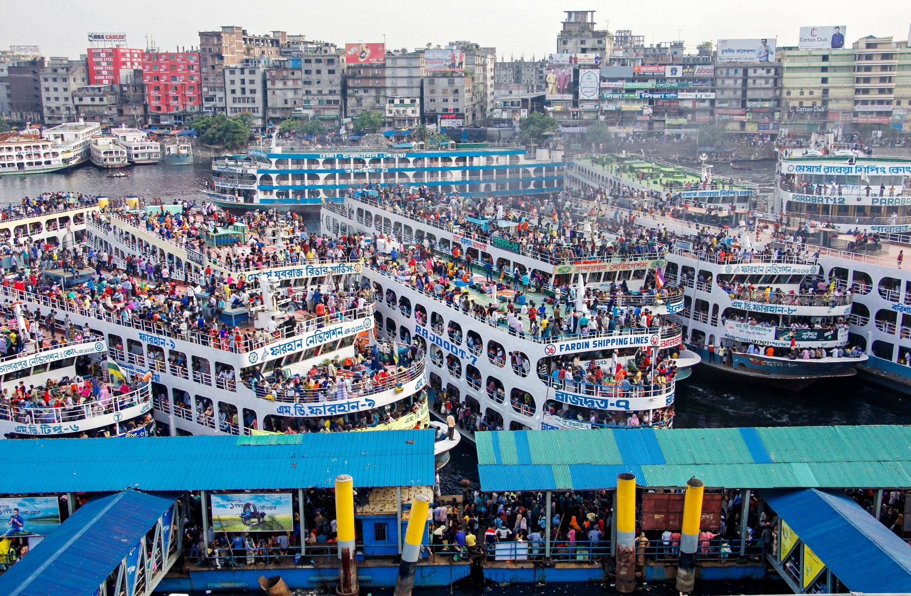 Crowds of wooden rowboats and multi-deck passenger paddle steamers crossing the busy brown waters of the Buriganga River at Sadarghat