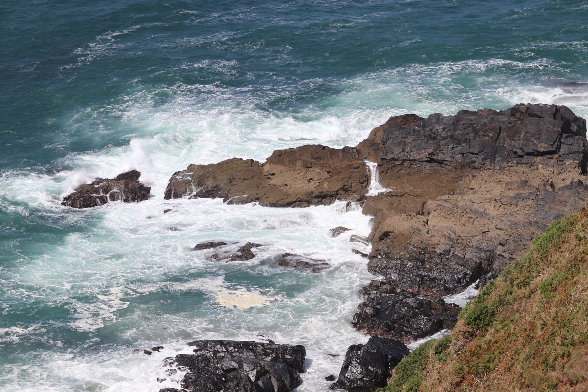 Towering coral limestone sea cliffs battered by massive white ocean swells under bright sunshine