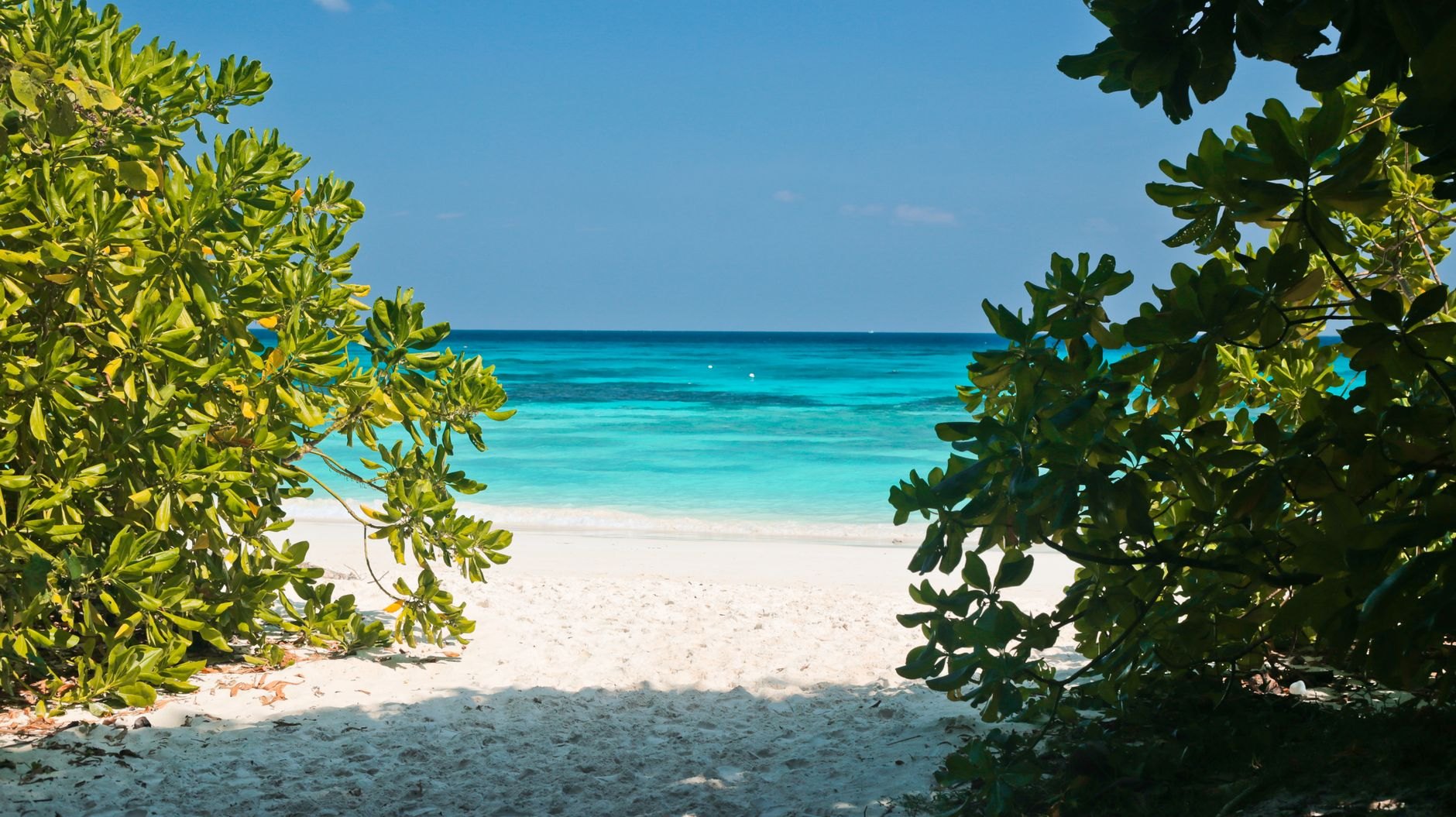 Crystal clear turquoise Caribbean water gently lapping wide white sands at Carlisle Bay with boats anchored in the distance