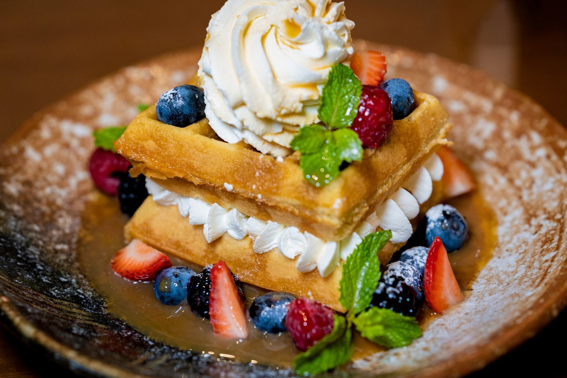 Fresh golden Brussels waffle dusted with powdered sugar and topped with fresh ripe strawberries and chocolate sauce