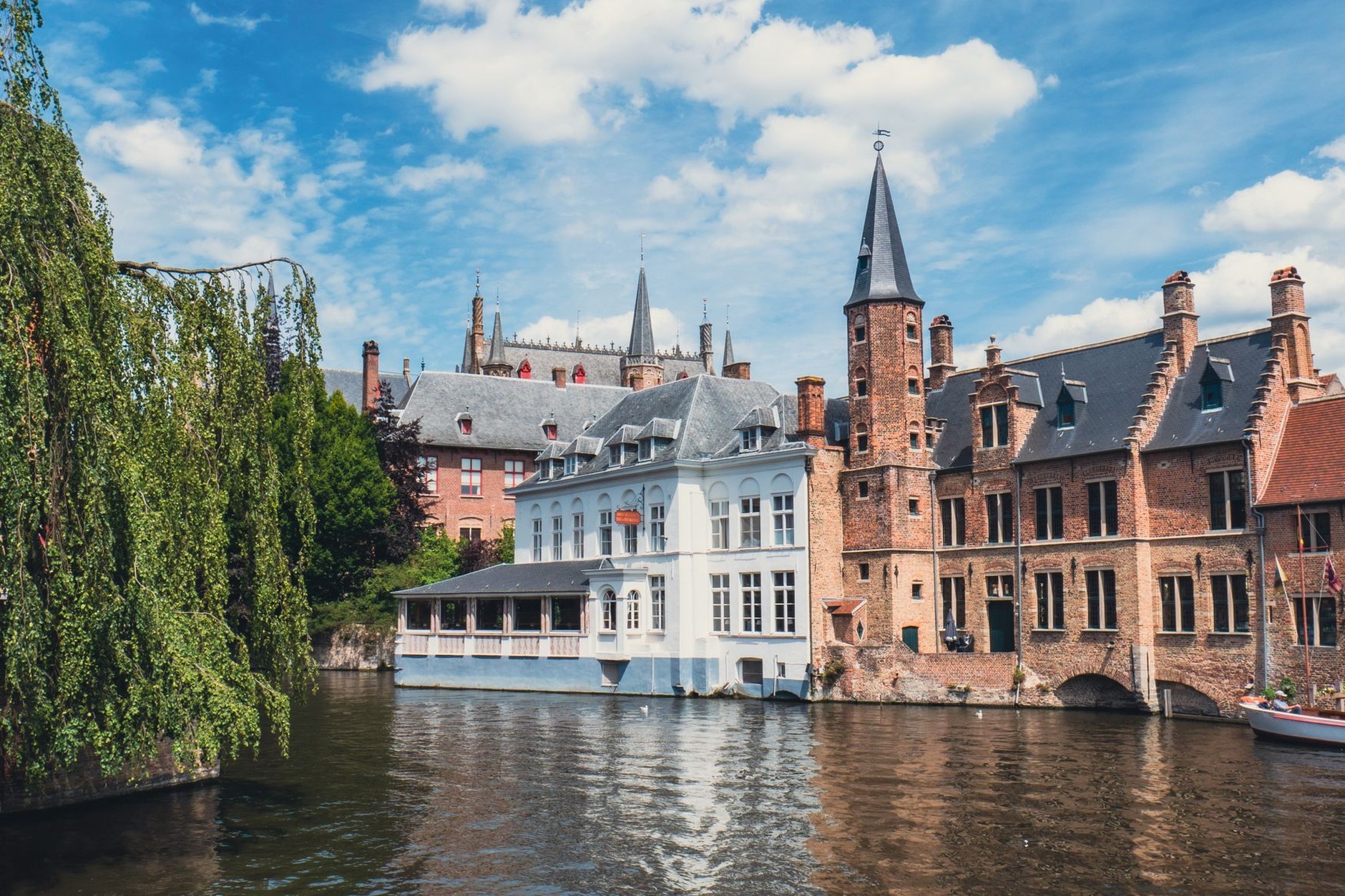 Classic canal viewpoint of Rozenhoedkaai in Bruges Belgium showing medieval spires and weeping willow over water