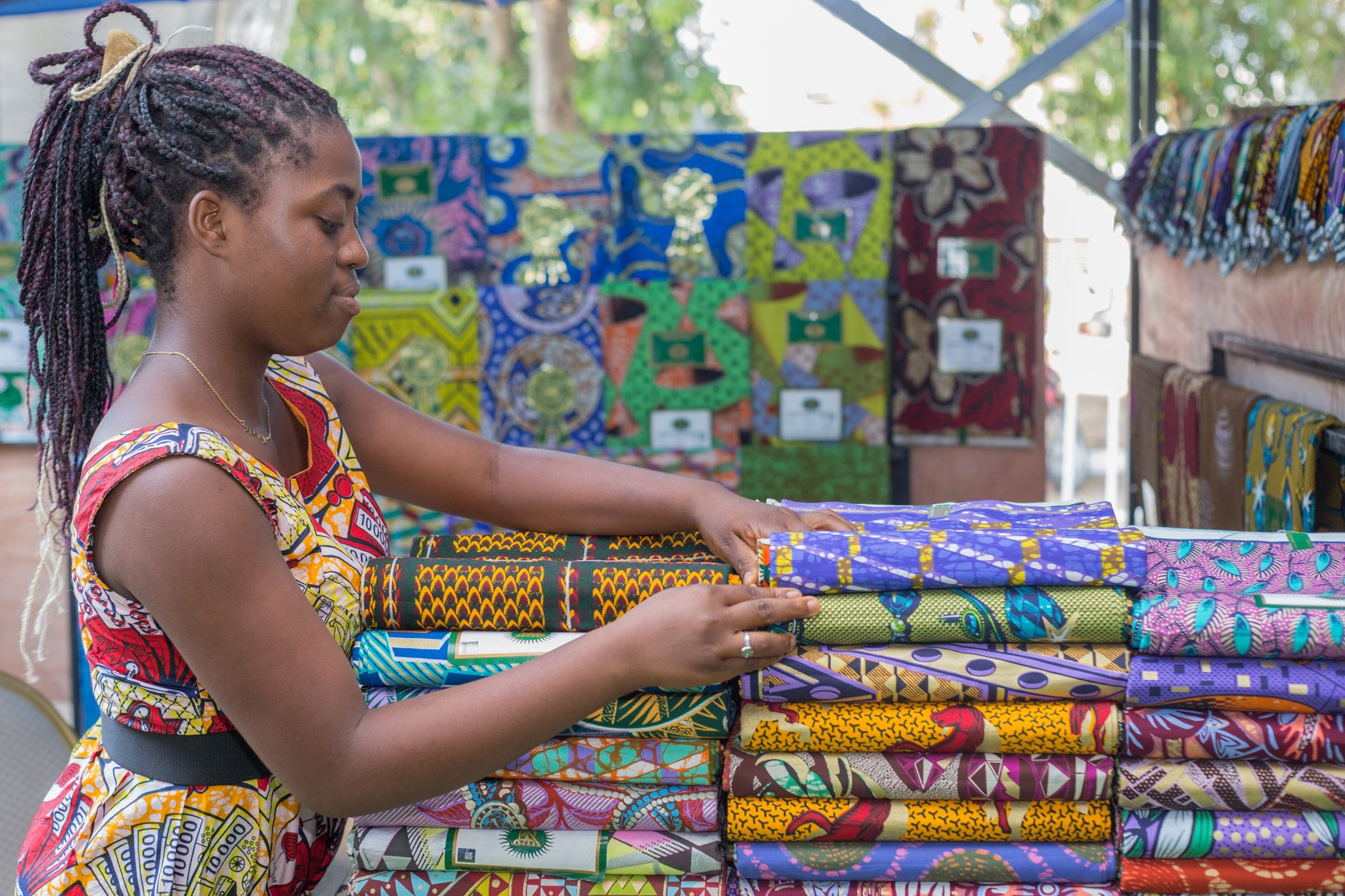 Market vendor organizing colorful wax print fabrics and textiles at Dantokpa market in Cotonou