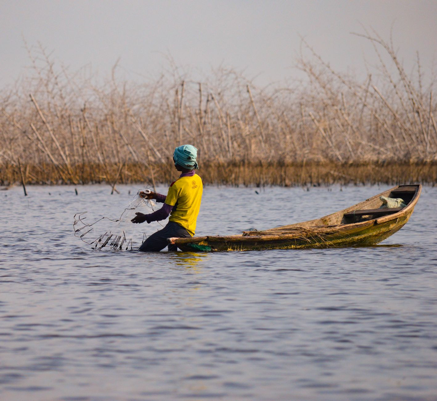 Fisherman casting a circular fishing net over Lake Nokoue from a slender wooden canoe