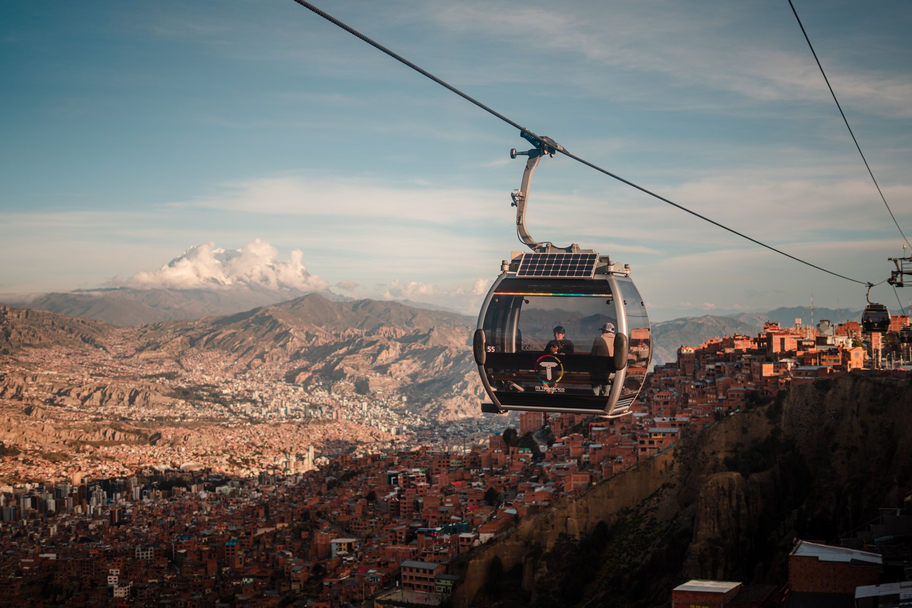 Mi Teleférico cable car cabin gliding high above the dense brick architecture of the La Paz canyon with snow-capped Mount Illimani in the background