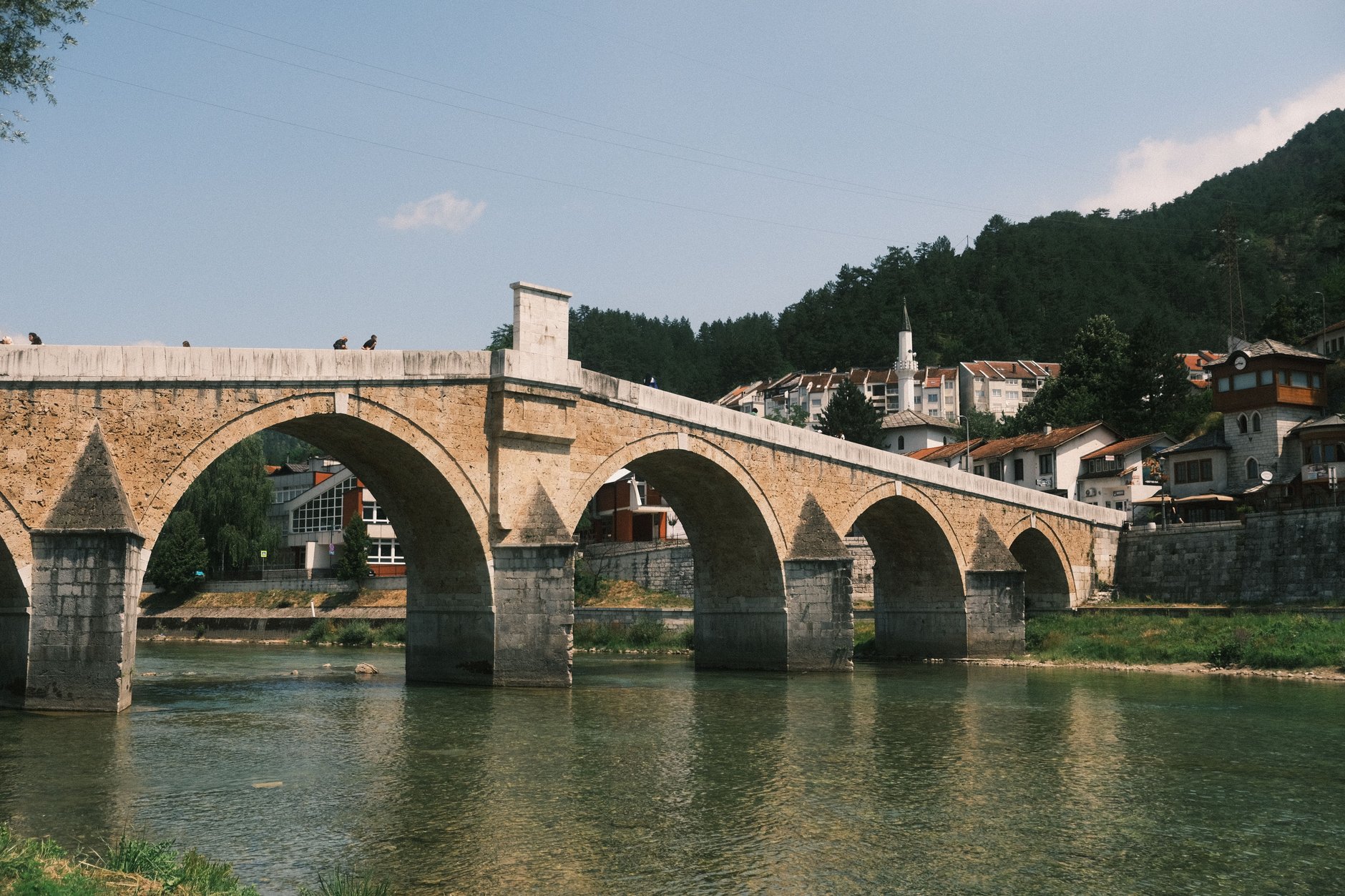 Six-arched Ottoman stone bridge of Konjic spanning the green waters of the Neretva River against towering mountain peaks