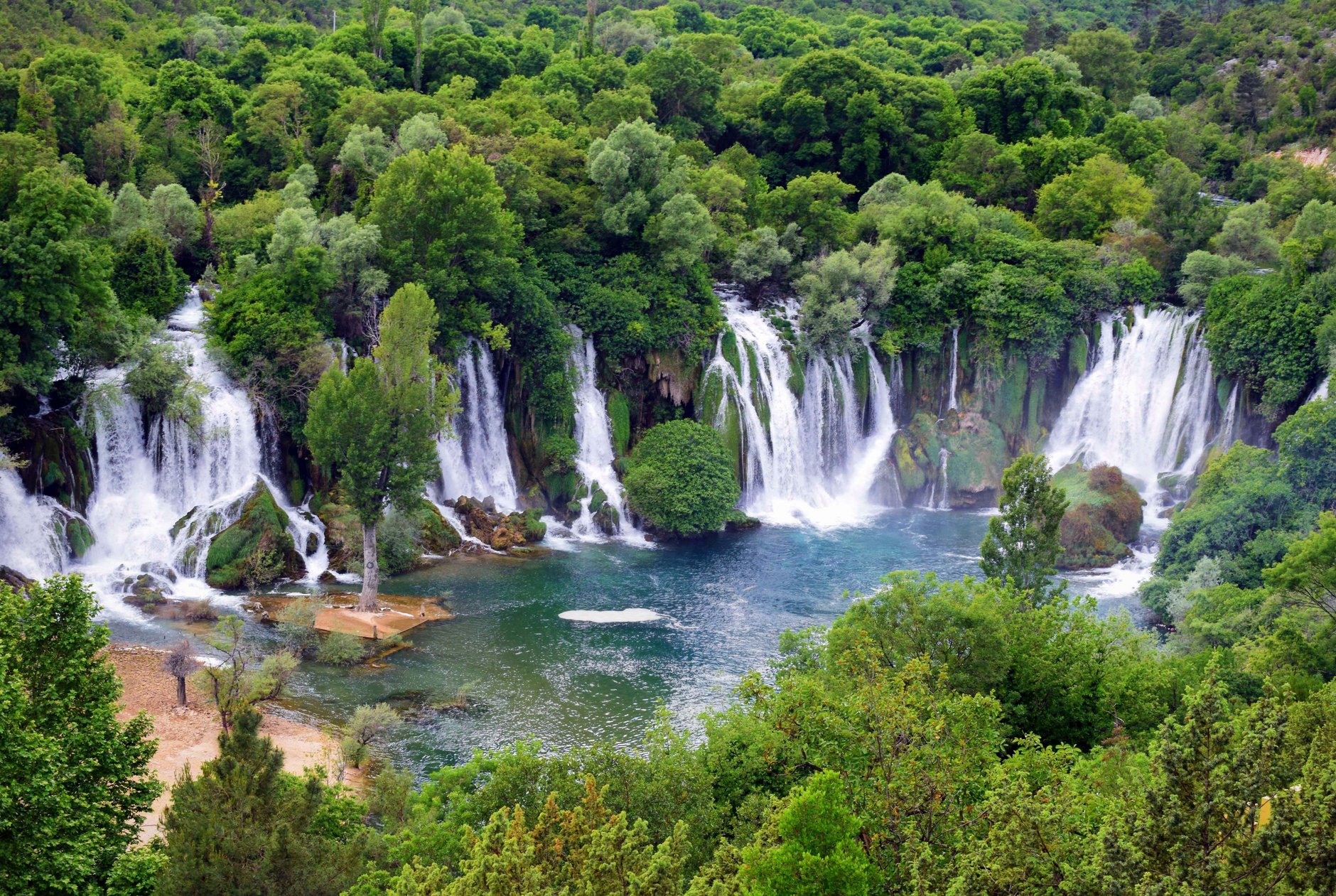 Wide natural travertine amphitheater of Kravica Waterfalls cascading twenty-five meters into a clear turquoise swimming lagoon