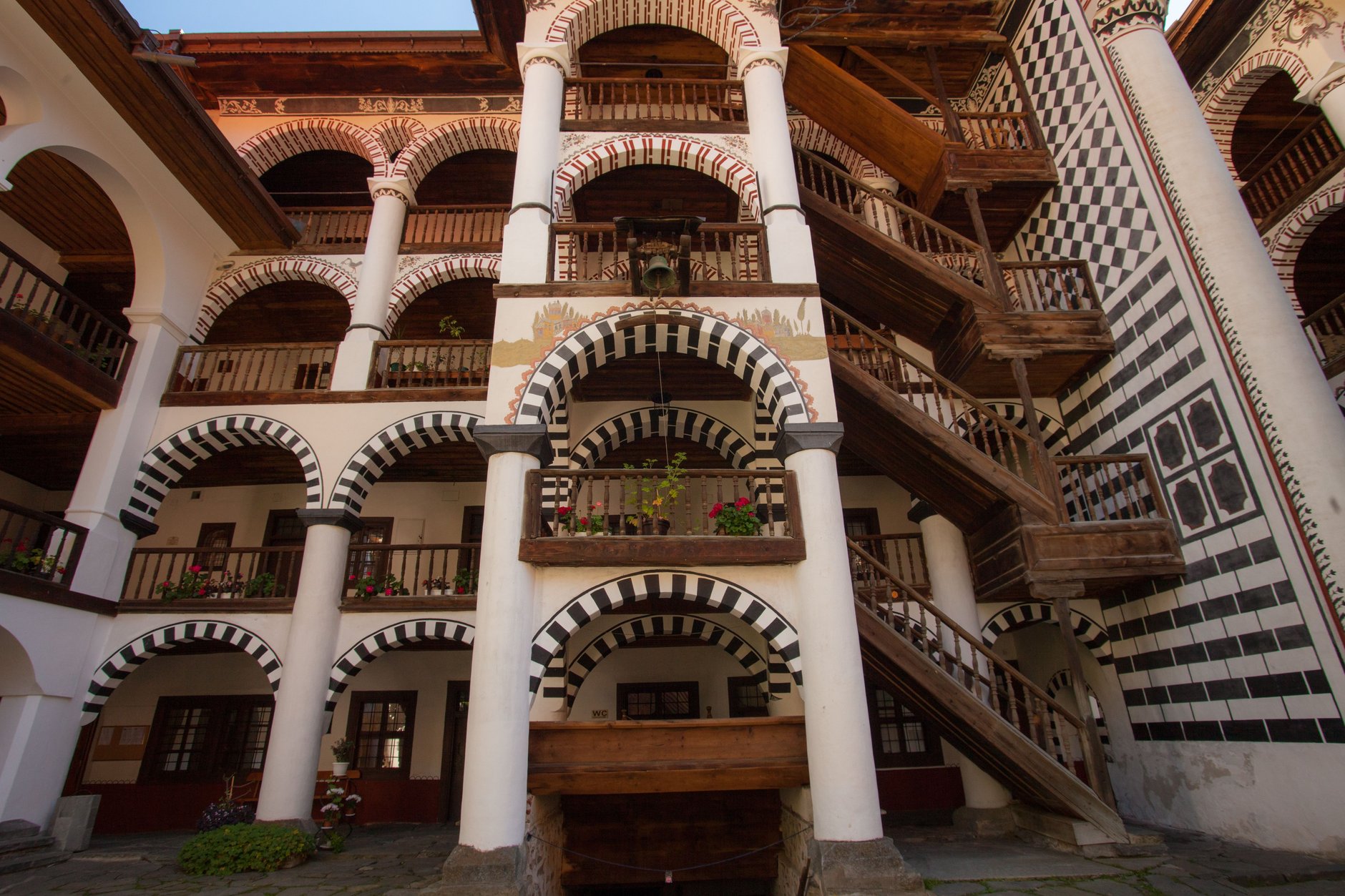Four tiers of striped black and white arched colonnades surrounding the courtyard of Rila Monastery with medieval Hrelyo Tower