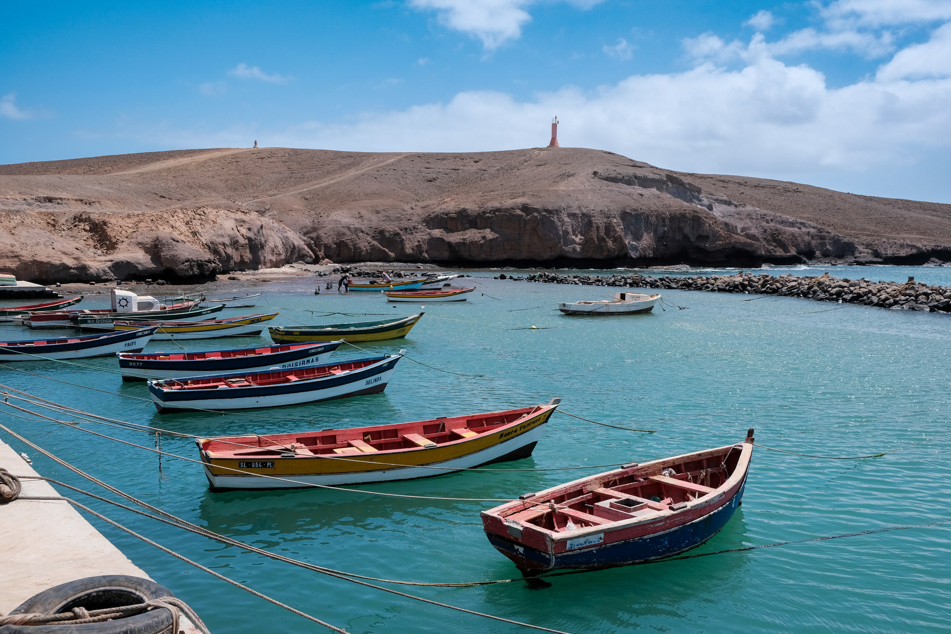 Brightly painted traditional wooden fishing boats anchored in clear coastal waters along an arid coastline